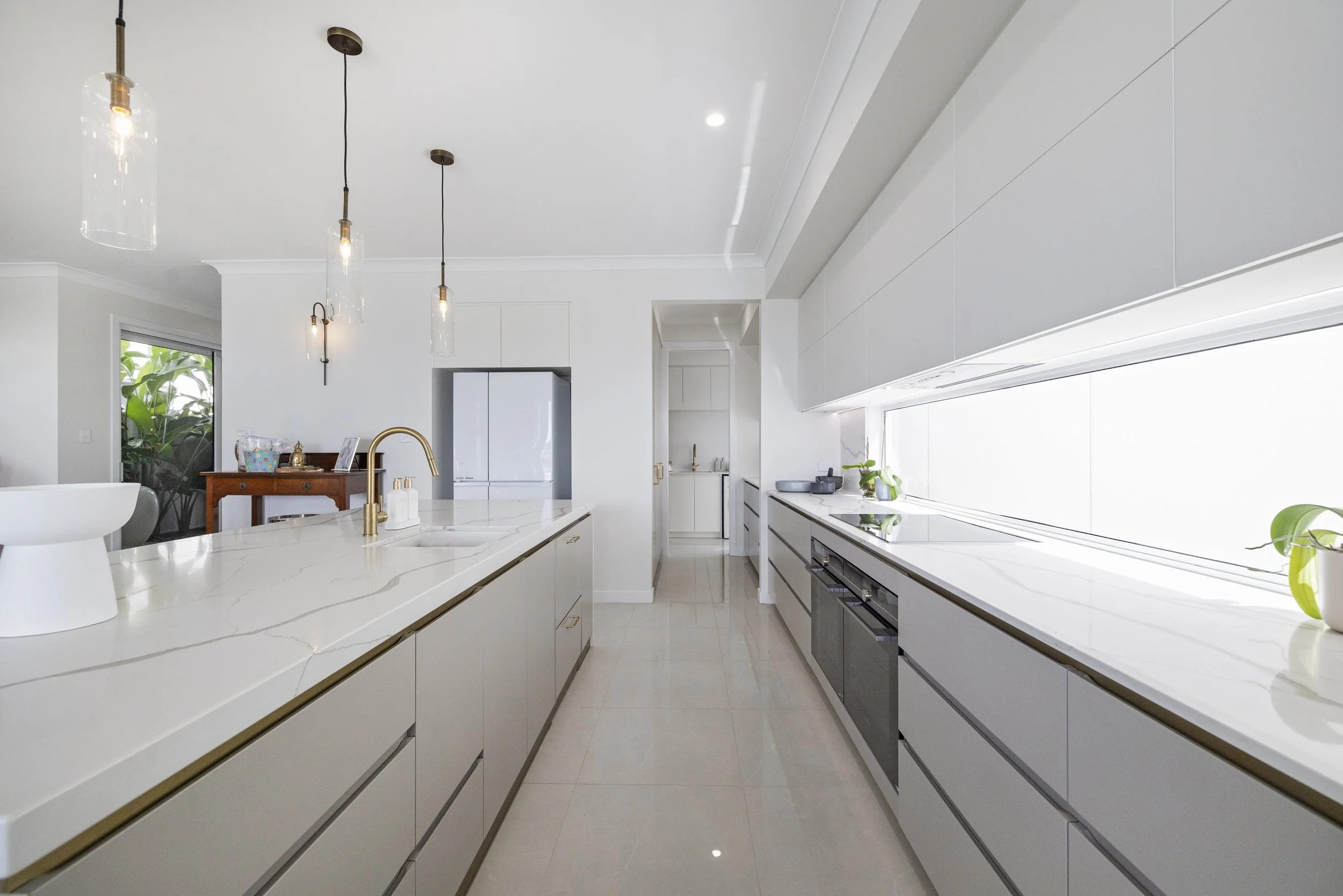 Modern kitchen with white cabinets, marble countertops, a large window, and pendant lighting fixtures.
