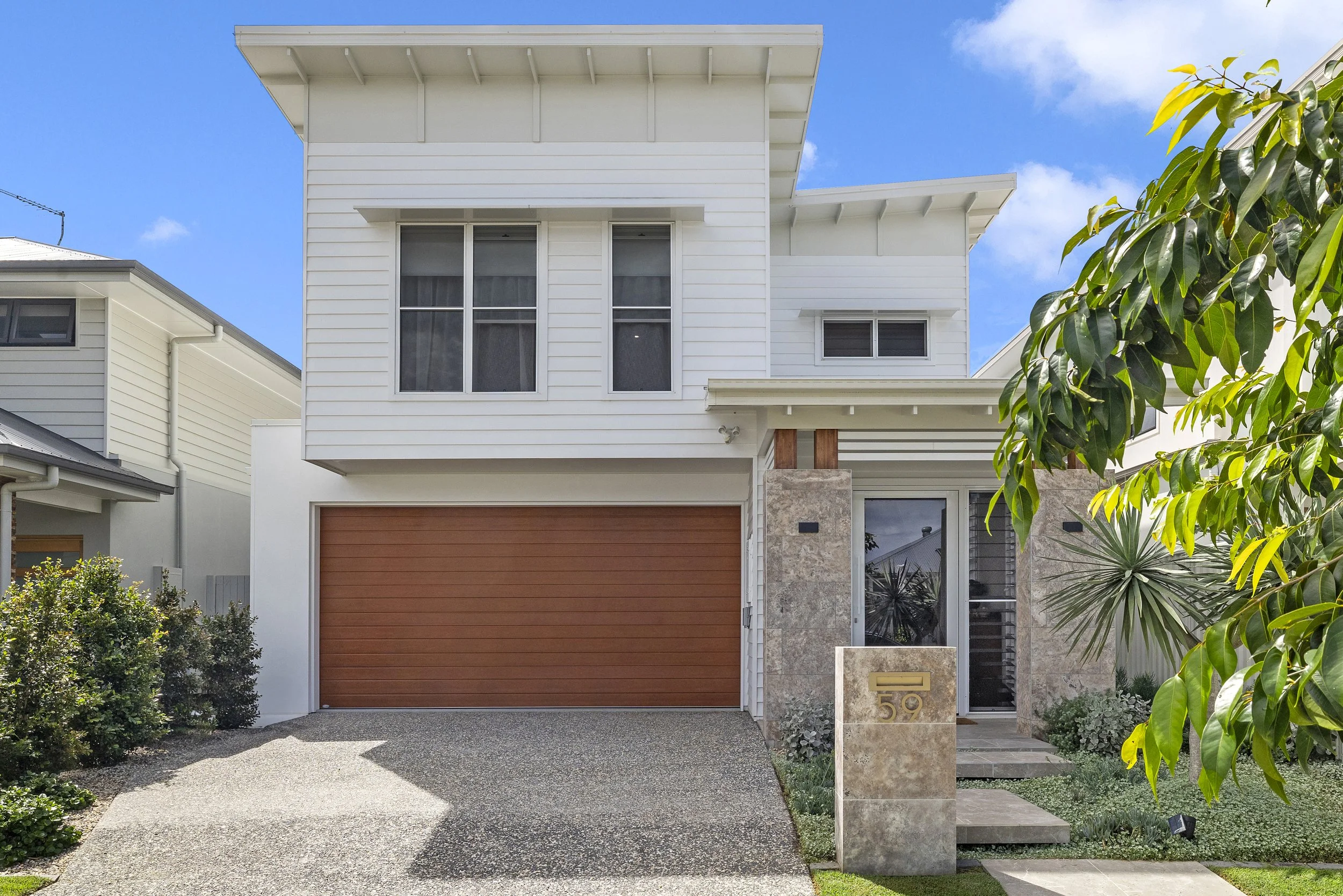 Front view of a modern two-story house with white siding, a brown garage door, and a landscaped entrance with a tiled porch, plants, and a house number 59.