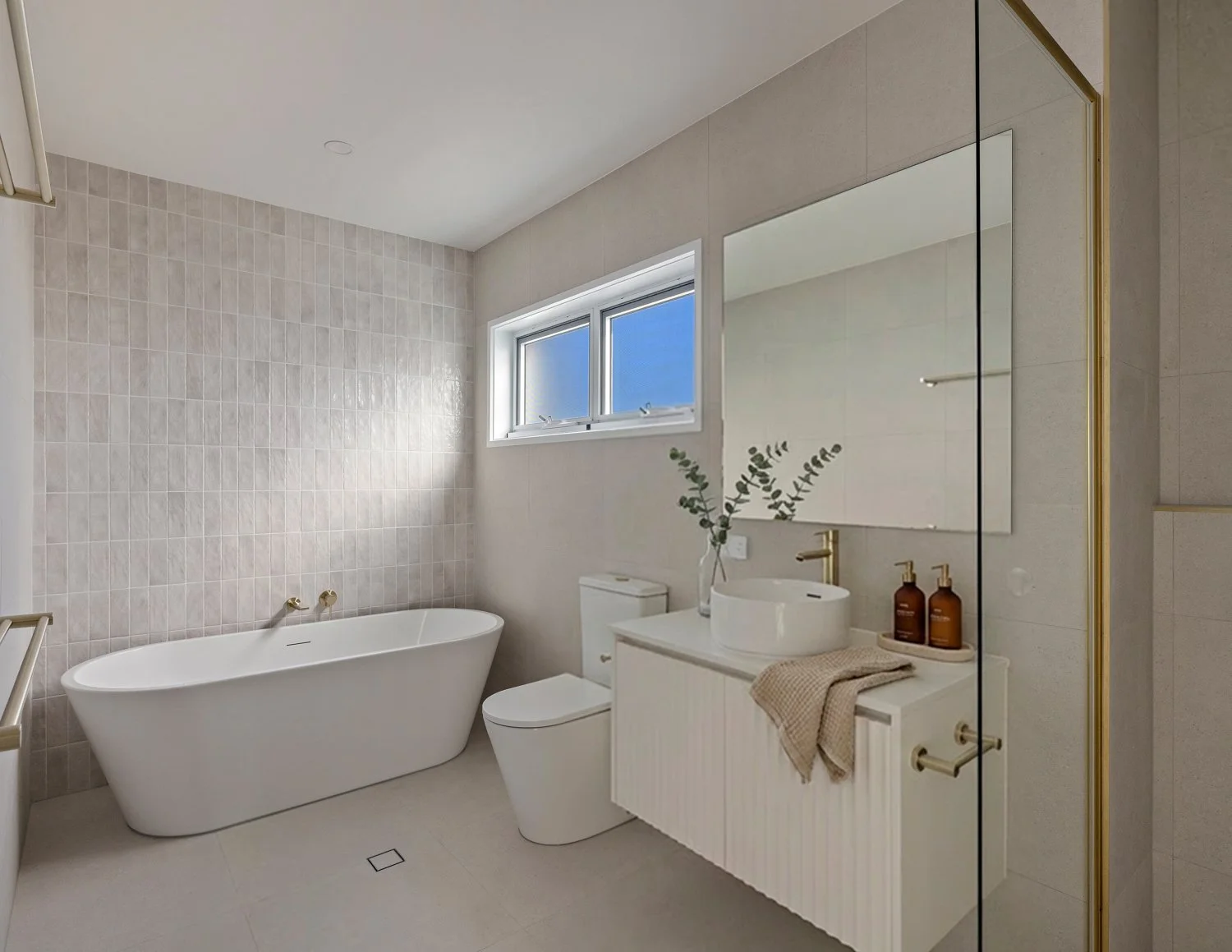 Modern bathroom with a freestanding bathtub, a toilet, a vanity with a vessel sink, and a large mirror. Light-colored tiles and a small window are on the wall.