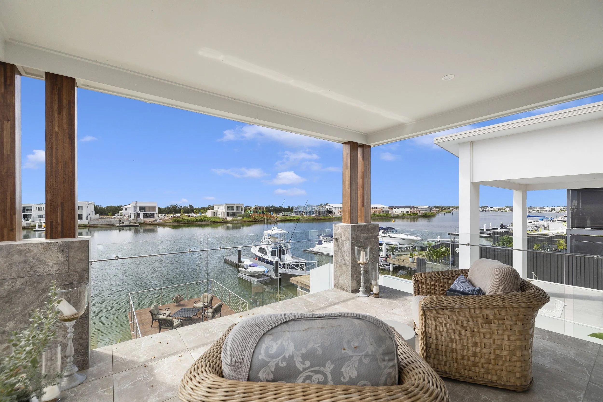 Balcony overlooking a marina with boats, modern houses, and a blue sky with clouds.