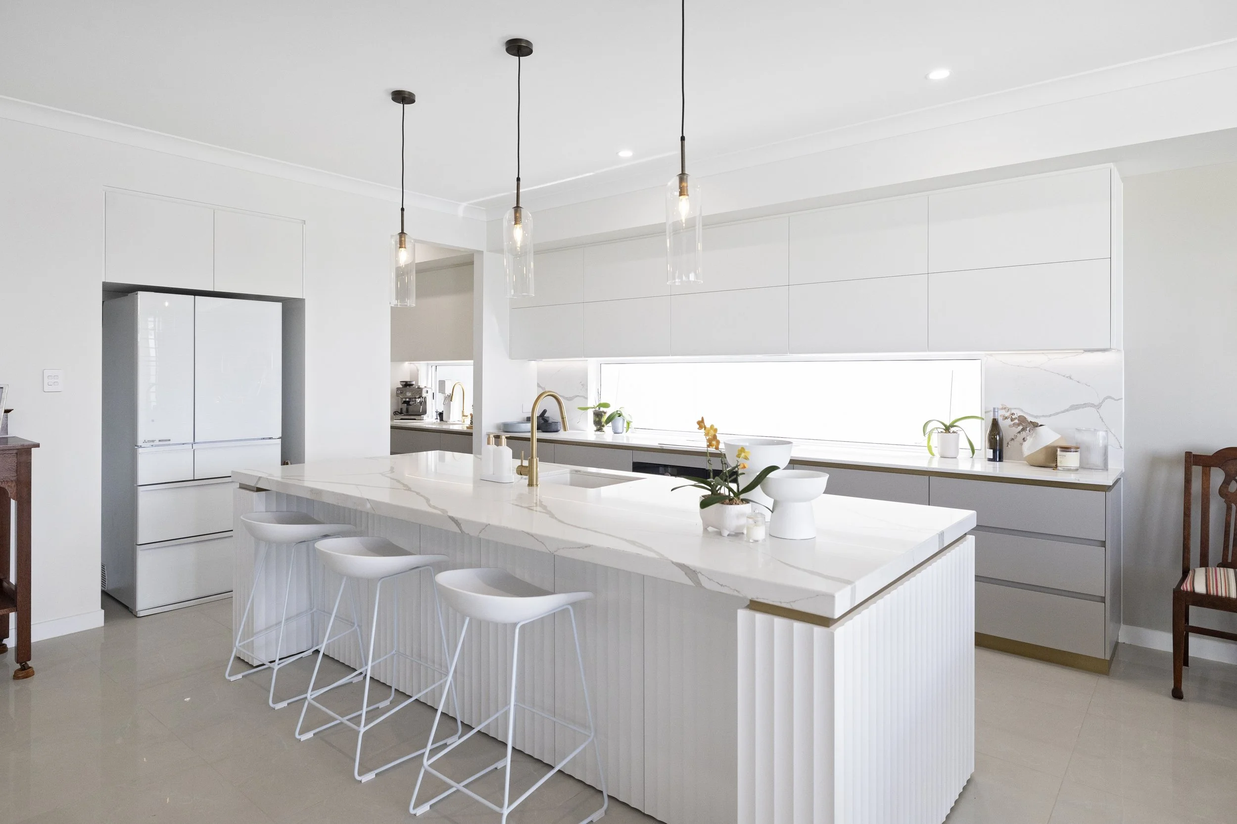 Modern white kitchen with a large island, pendant lights, and clean cabinetry.