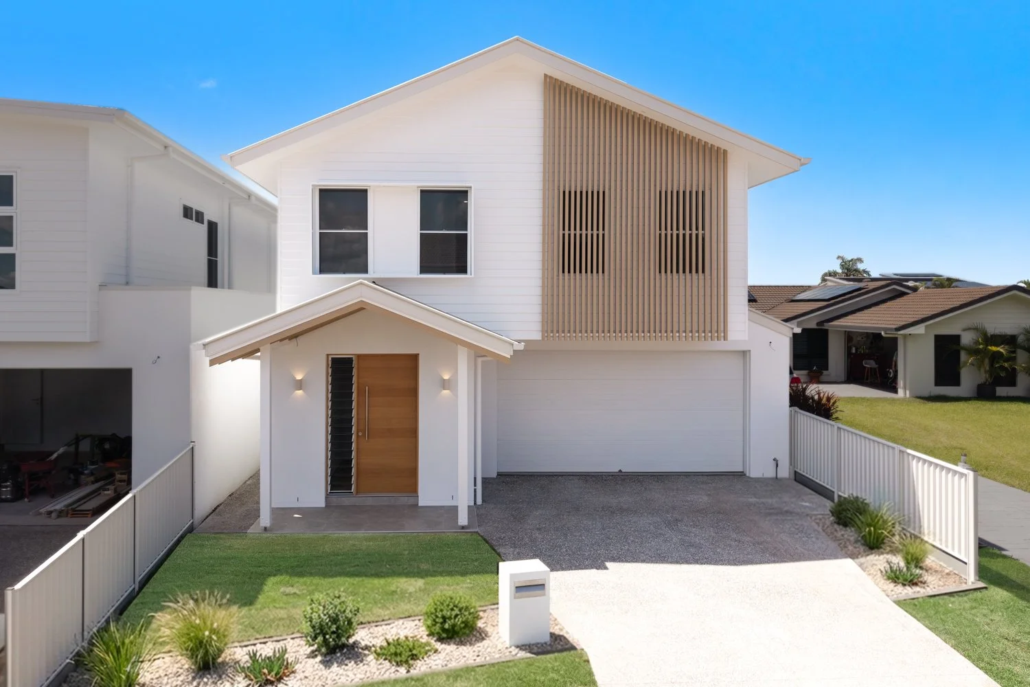 Modern two-story white house with wooden accents, a small front lawn, and a driveway with a garage door