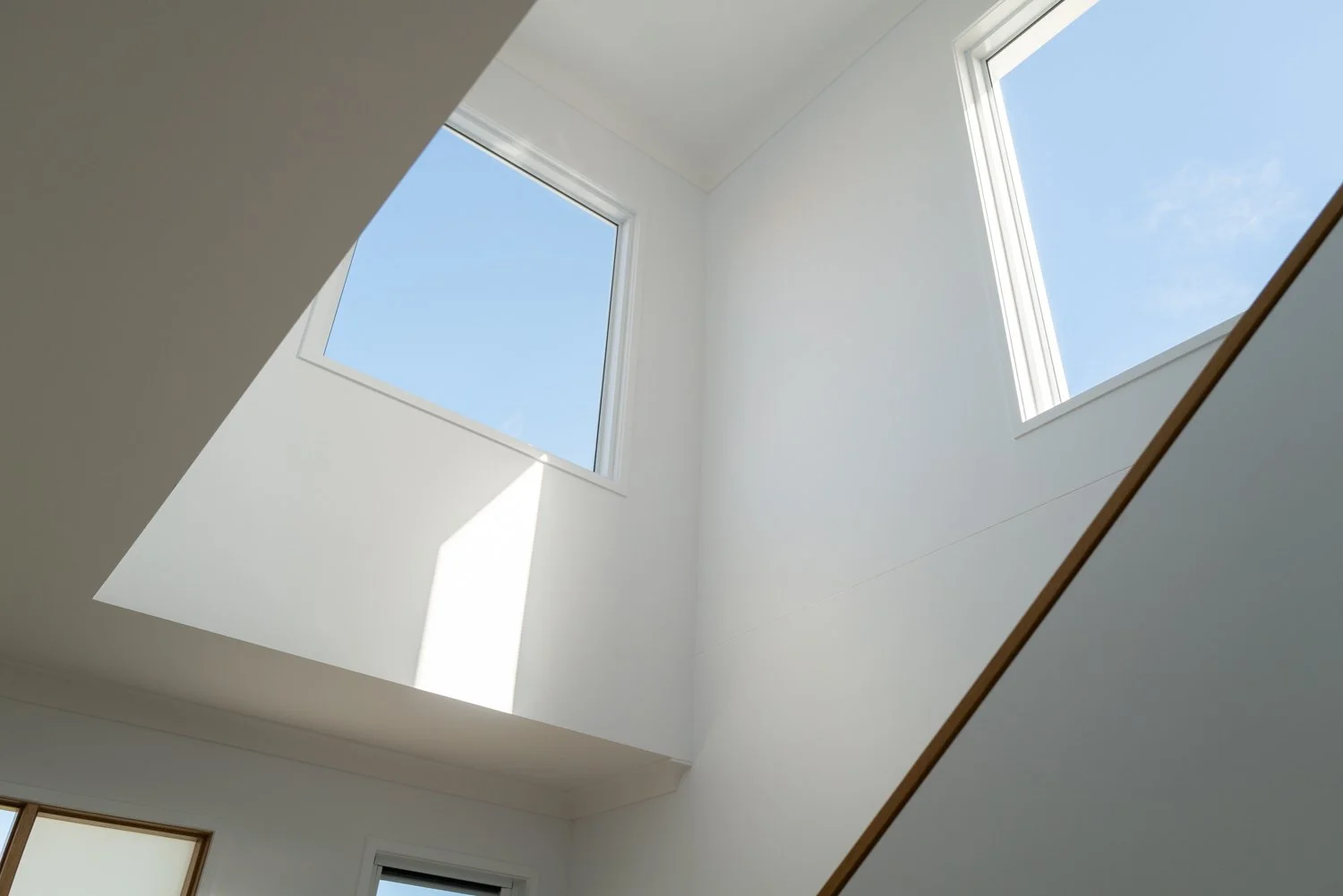 Interior view of a white ceiling with two large rectangular skylights showing blue sky and some clouds, sunlight casting shadows inside.