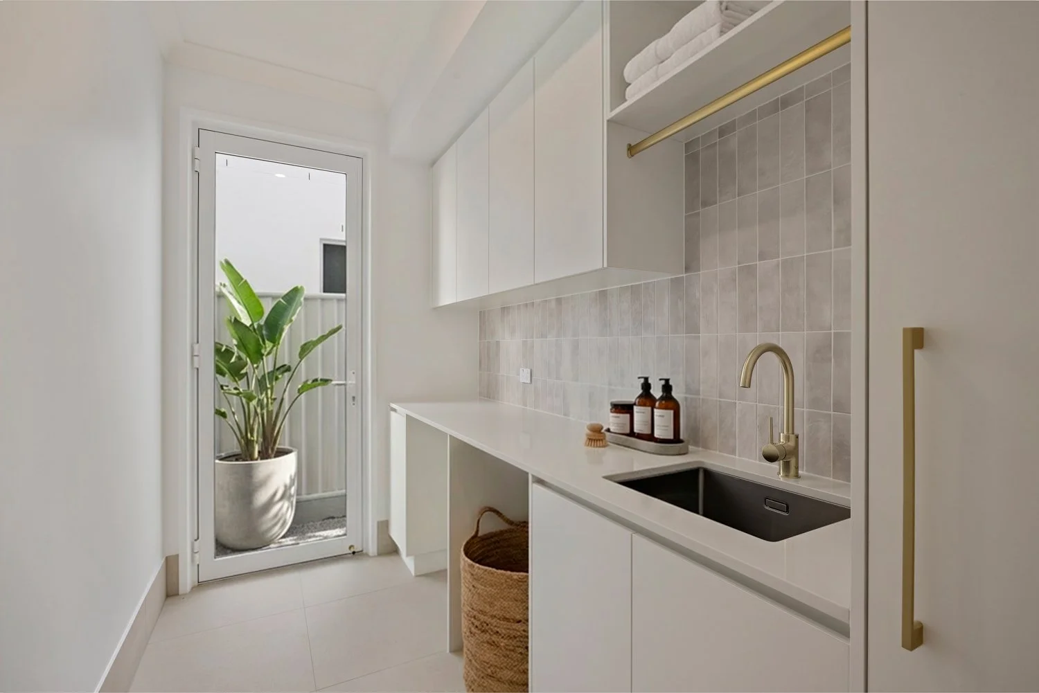 Modern laundry or utility room with white cabinets, beige tile backsplash, black sink, gold faucet, and a potted plant outside the door.