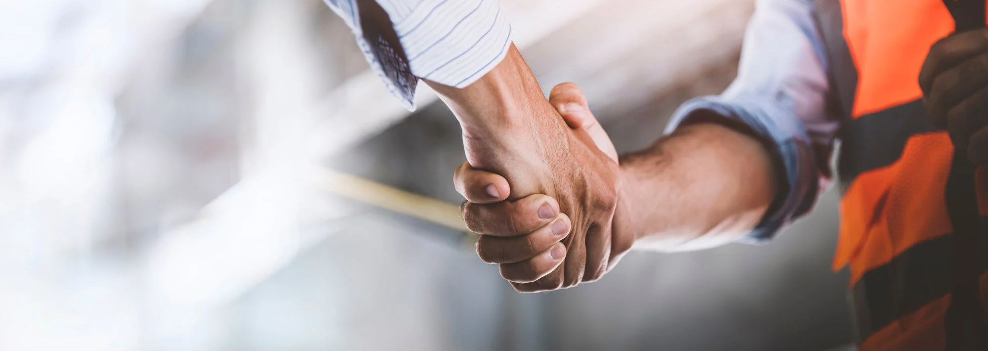 Two people shaking hands, one wearing a white shirt and the other wearing an orange safety vest, symbolising agreement.