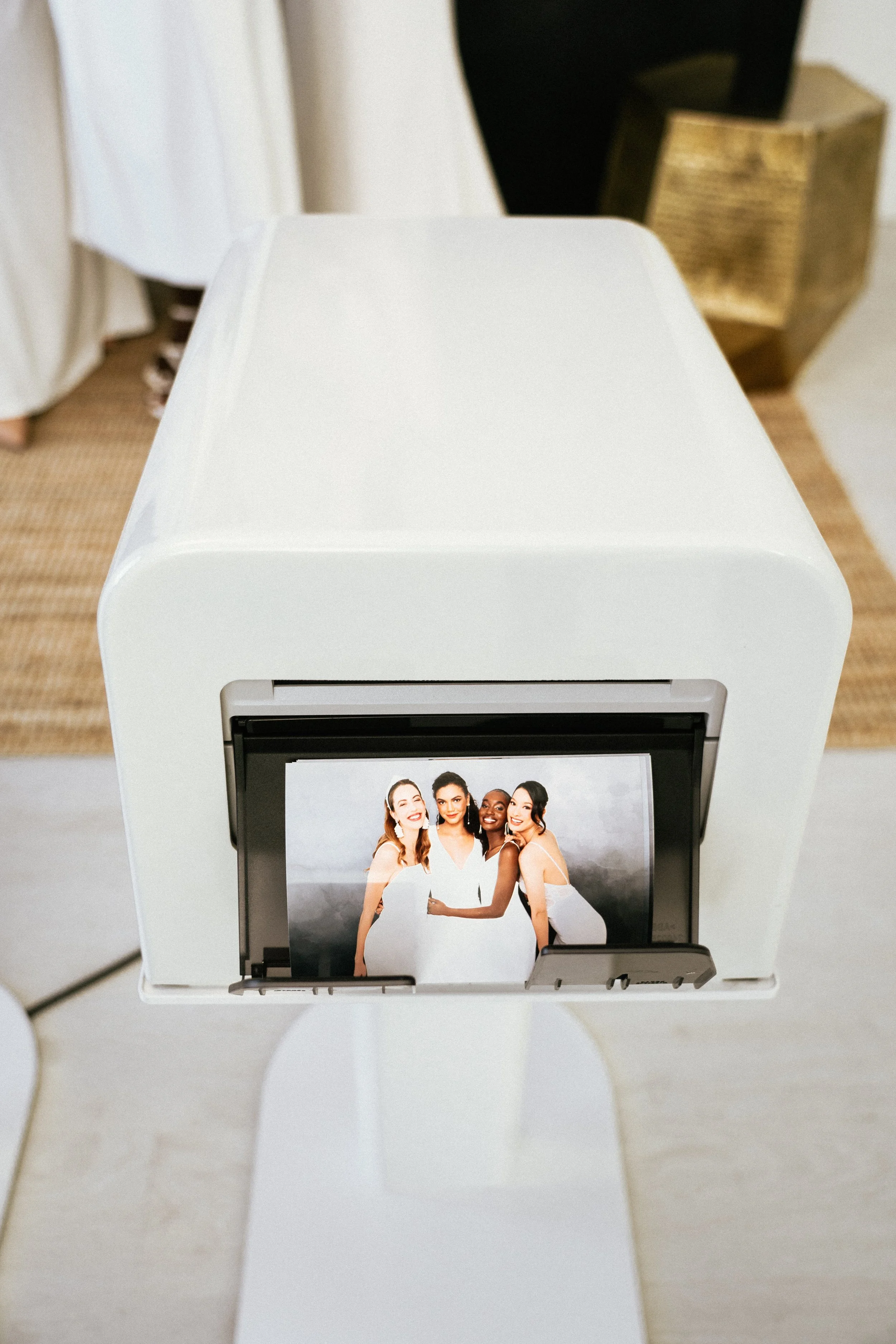A photo booth printing a picture of four women dressed in white, smiling and posing together.