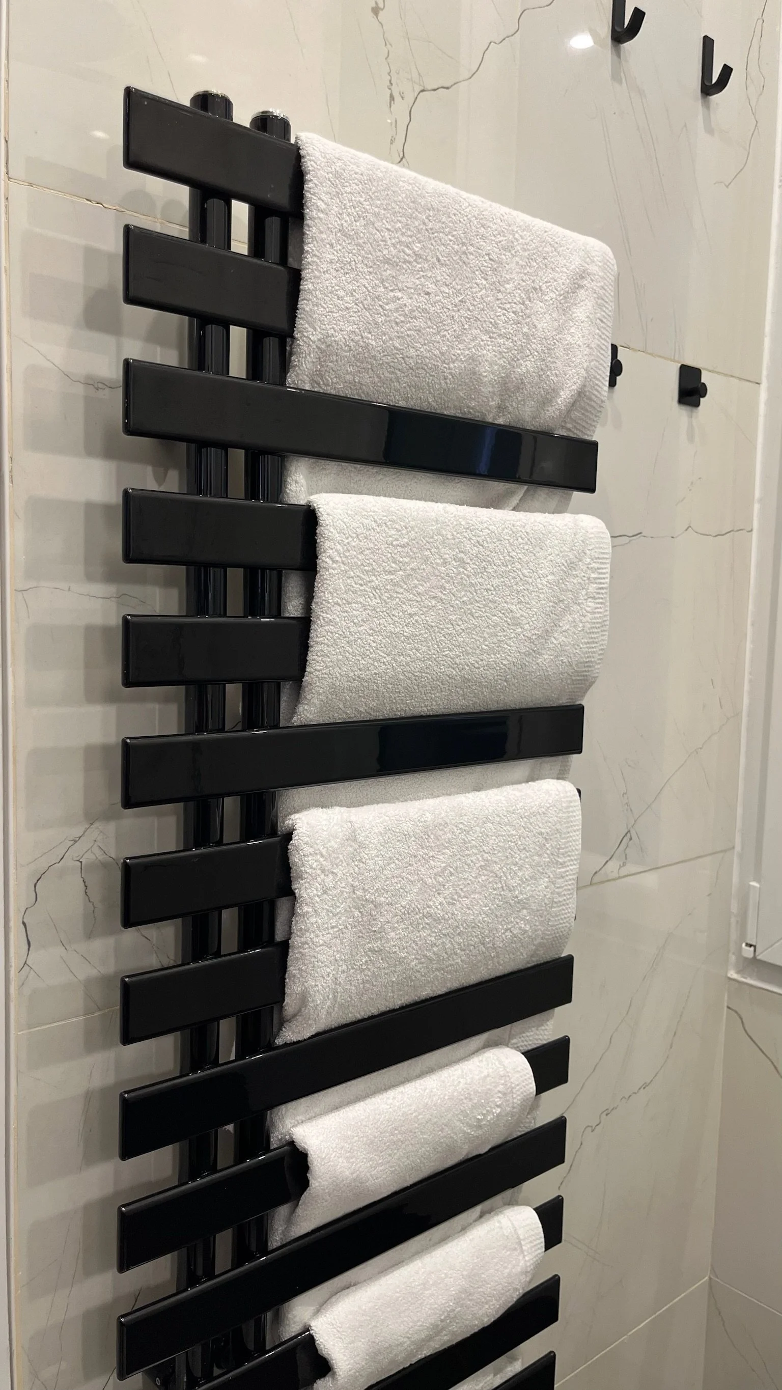 Black towel rack mounted on a tiled wall holding a row of white folded towels.