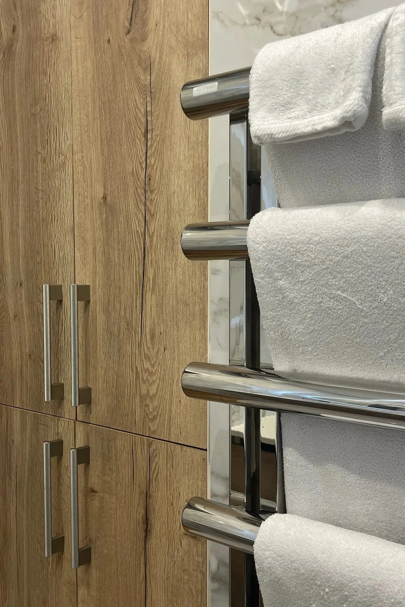Close-up of a towel rack with rolled white towels, mounted on a wooden cabinet with silver handles.