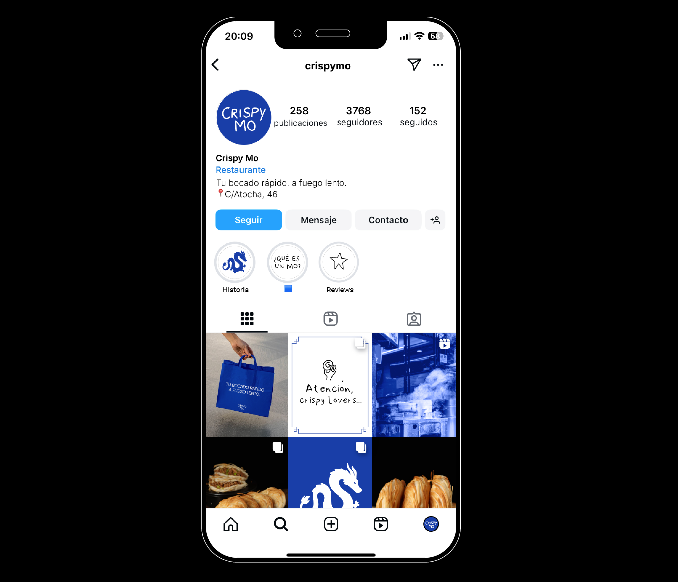 Pantalla de un teléfono móvil mostrando la cuenta de Instagram de 'Crispy Mo', un restaurante con publicaciones, seguidores y fotos de comida y promociones.