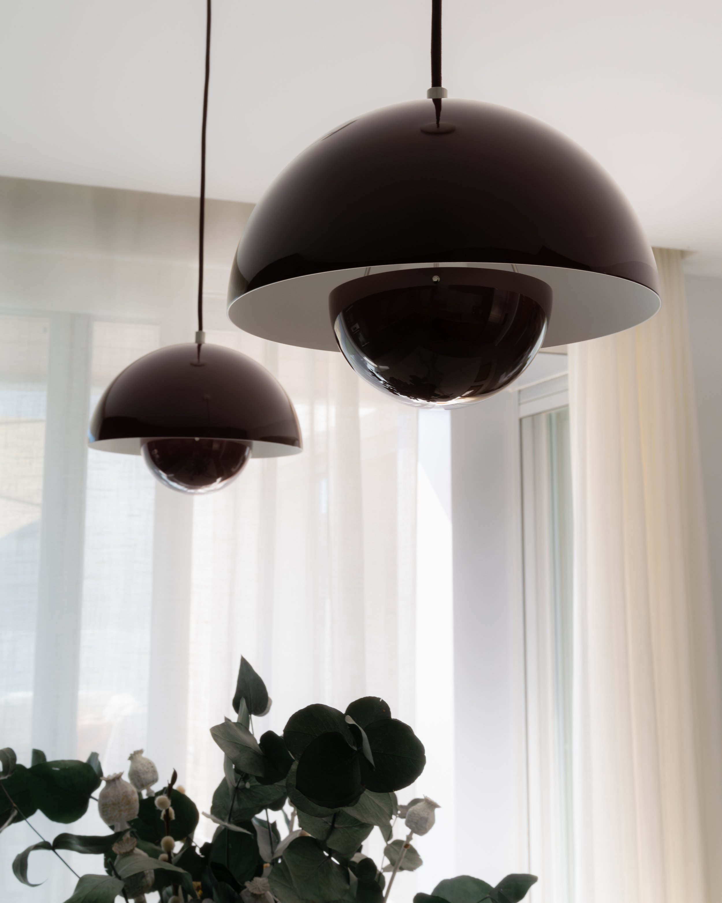 Lámpara moderna negra y blanca suspendida del techo en una habitación con cortinas blancas y plantas de interior debajo