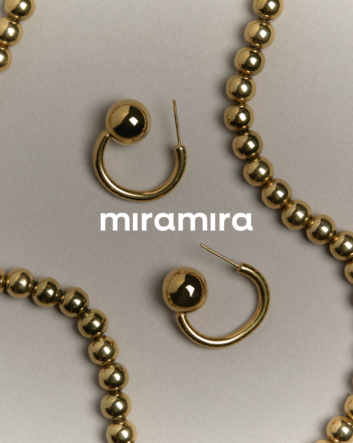 Conjunto de joyería de pendientes de aro y collar de bolitas doradas en fondo gris claro.
