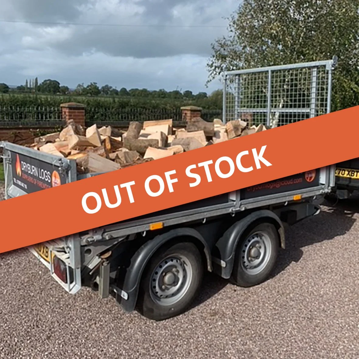 Trailer loaded with chopped firewood, marked "DRYBURN LOGS, Suppliers of Firewood," on a rural road.