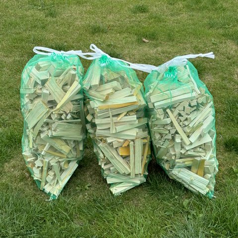 Bundles of green wood kindling sticks in netted bags with ties.