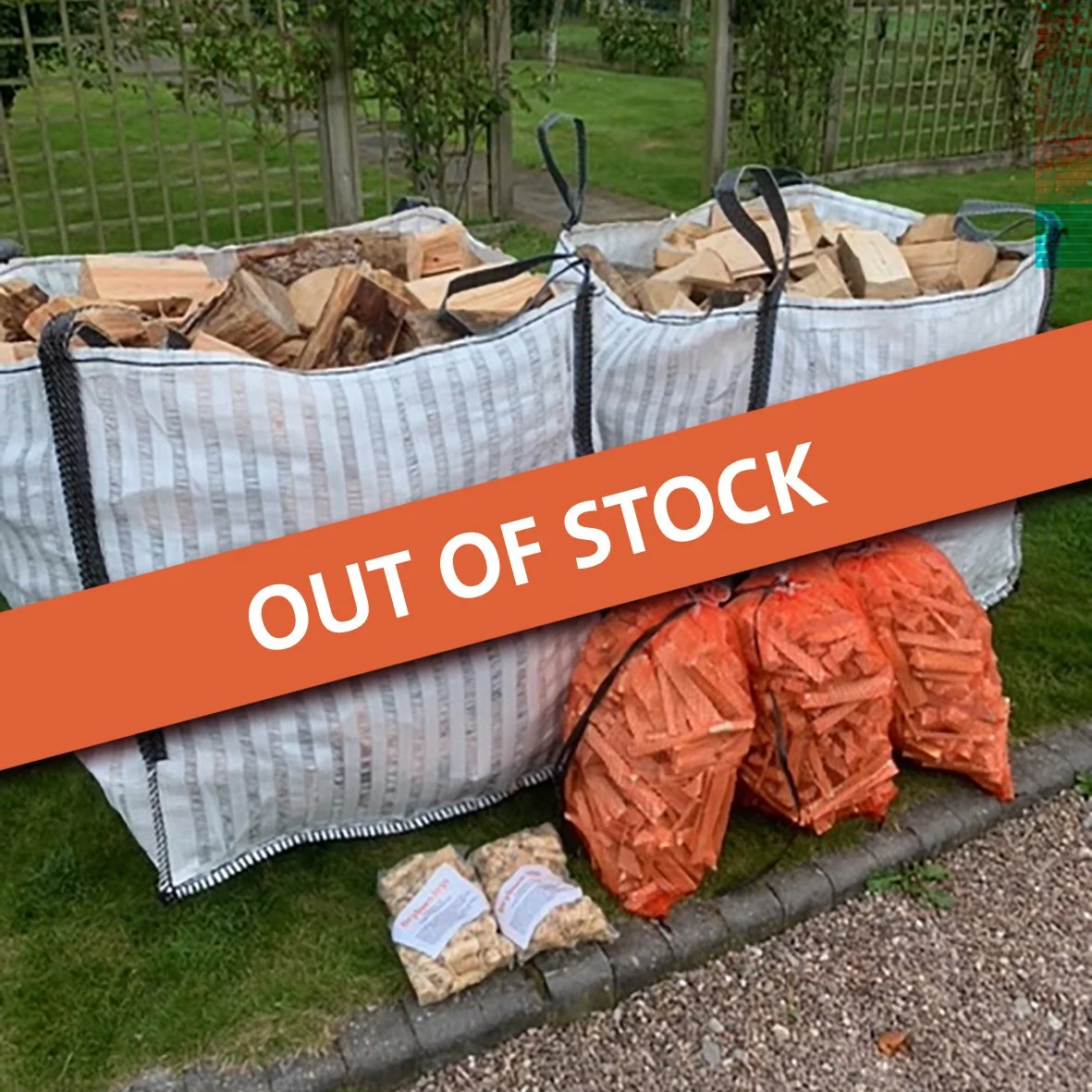 Two large bags of firewood labeled 'DRYBURN LOGS' are placed outside in a garden setting. The bags contain chopped logs and have contact information printed on them. Nearby are two green bags filled with kindling and a smaller bag of wood shavings, all arranged on a stone pathway.