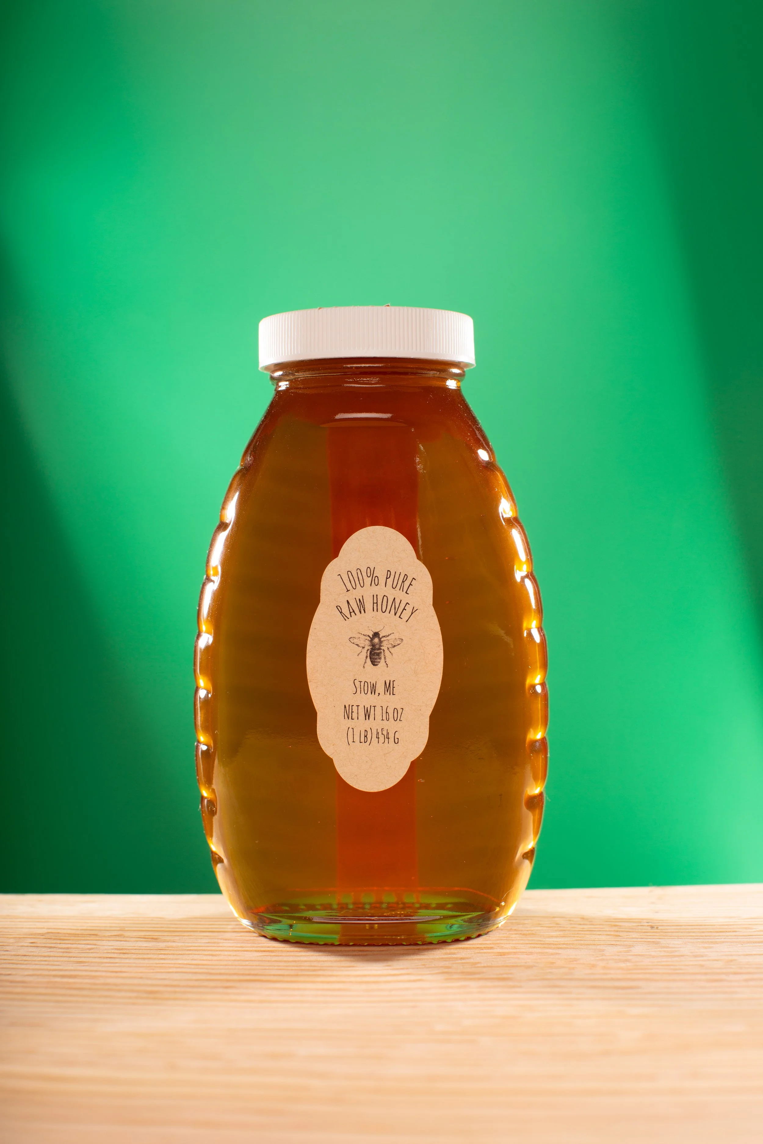Jar of pure raw honey with a white lid and label, set against a green background.