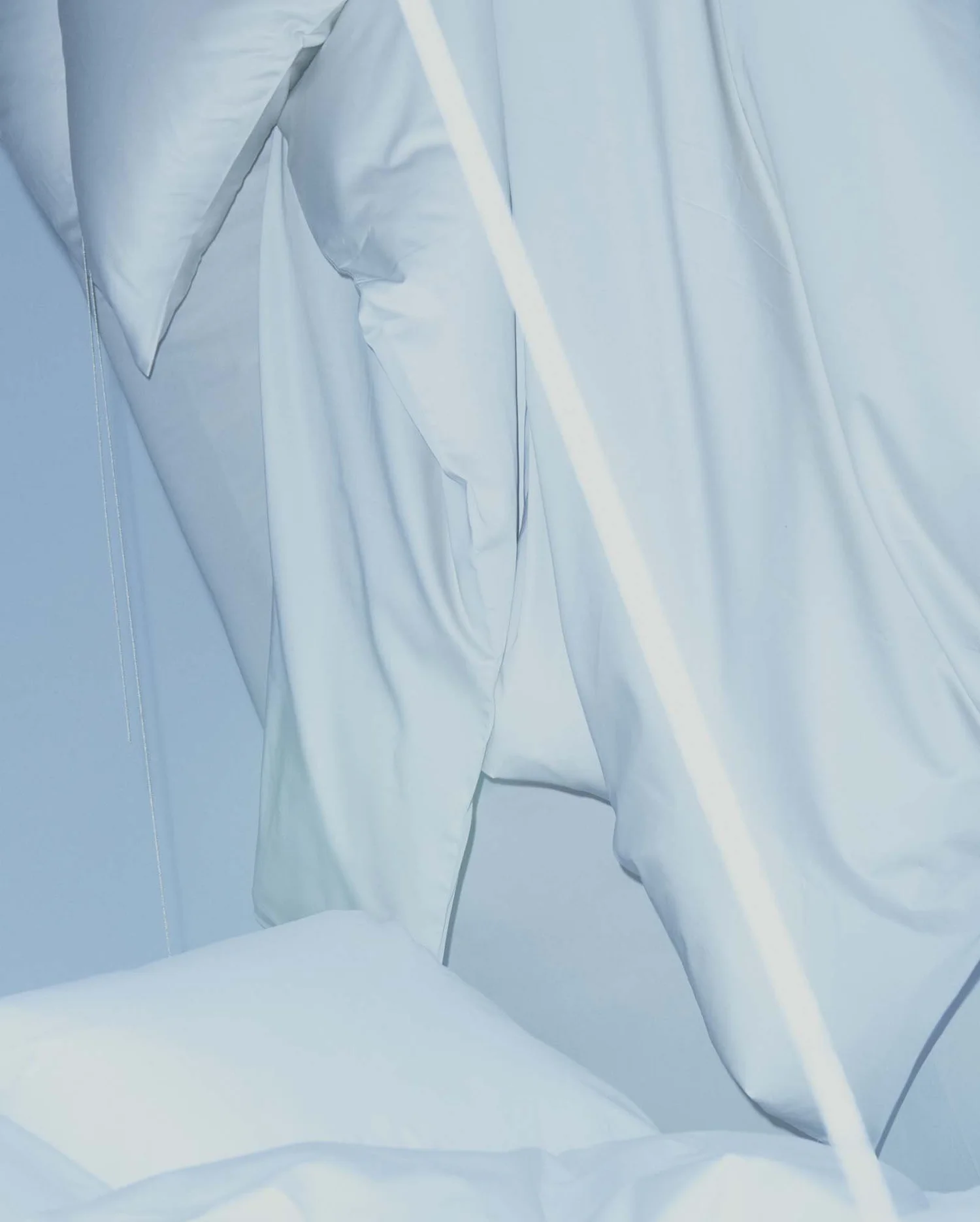 A close-up of pale blue bedding, folded fabric and stitched seams.