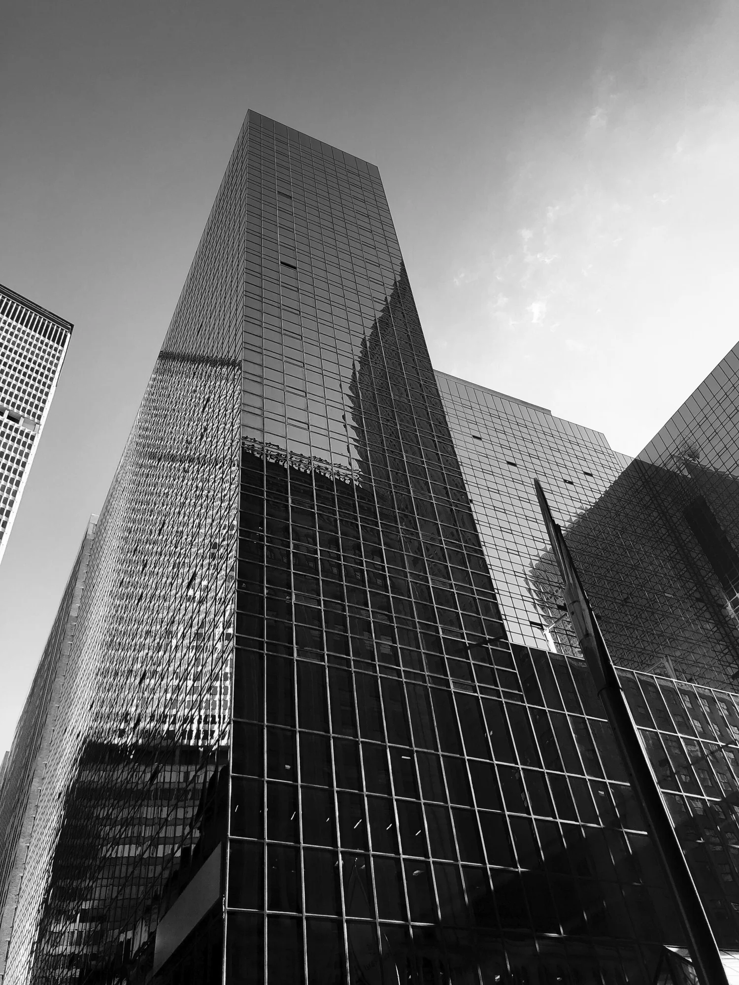 Black and white photograph of modern glass skyscrapers reflecting other buildings in a cityscape.