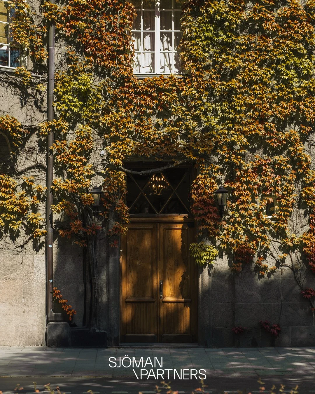 Sjöman Partners wordmark beneath a doorway framed by autumn foliage