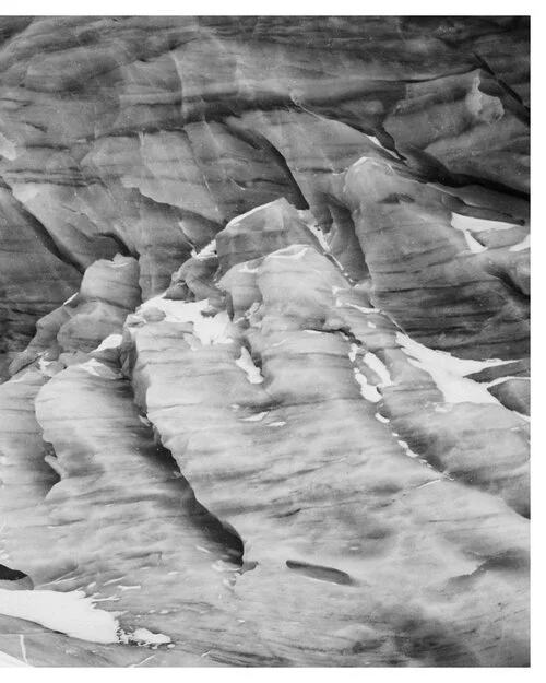 Black and white photograph of a glacier's ice with visible crevices and layers.