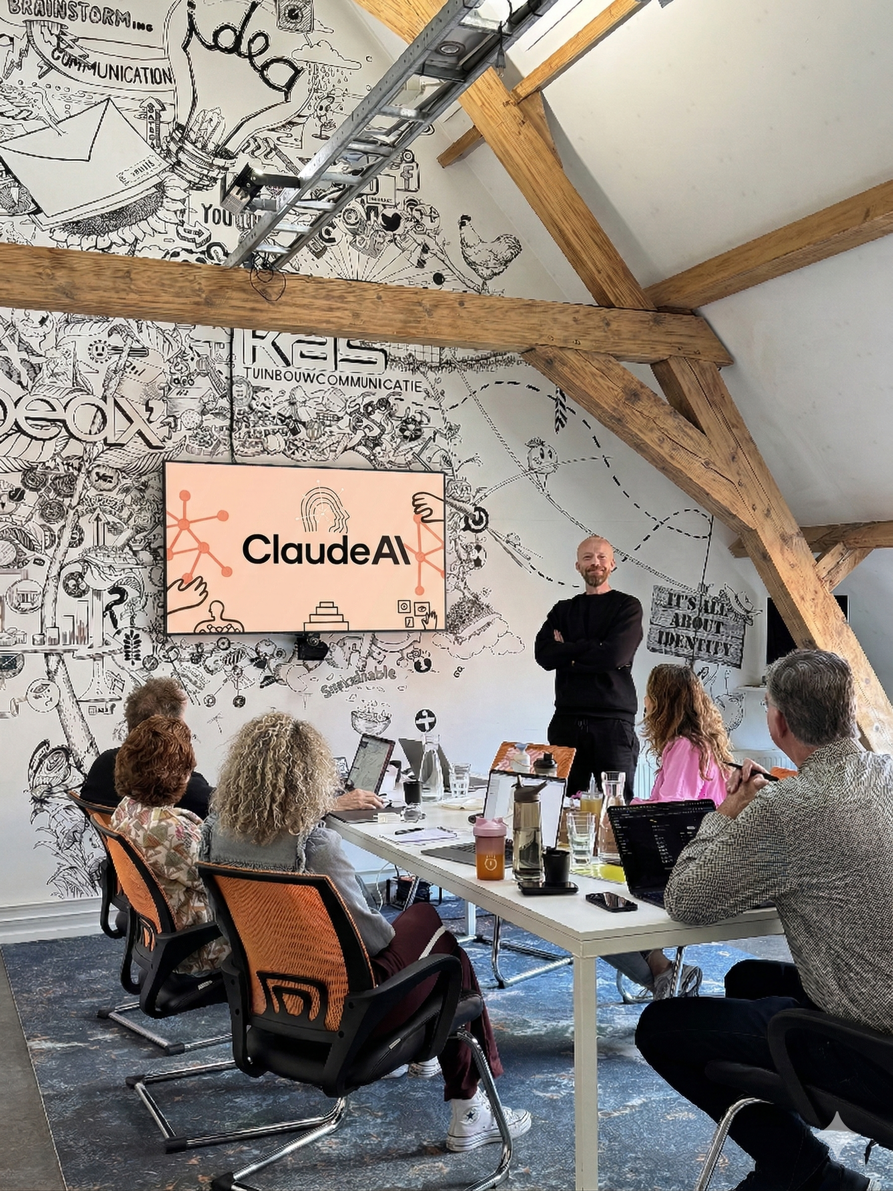 Een groepsvergadering in een vergaderruimte met een presenter die voor een scherm staat waarop 'ClaudeAI' staat. Mensen zitten aan een tafel met laptops en drinken. De muur is bedekt met zwarte en witte illustraties en teksten.