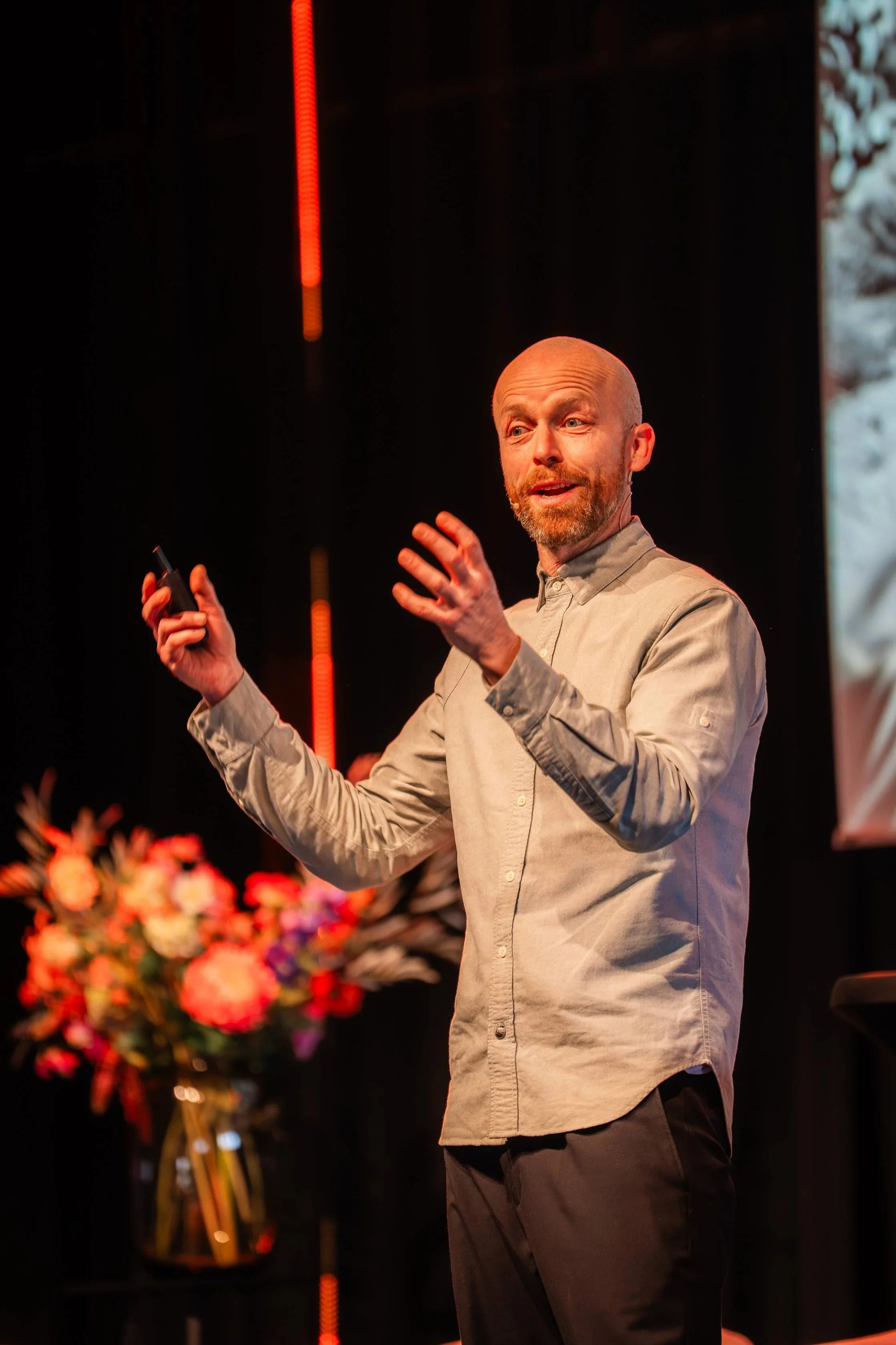 Man geeft een presentatie op een podium met bloemen op de achtergrond.