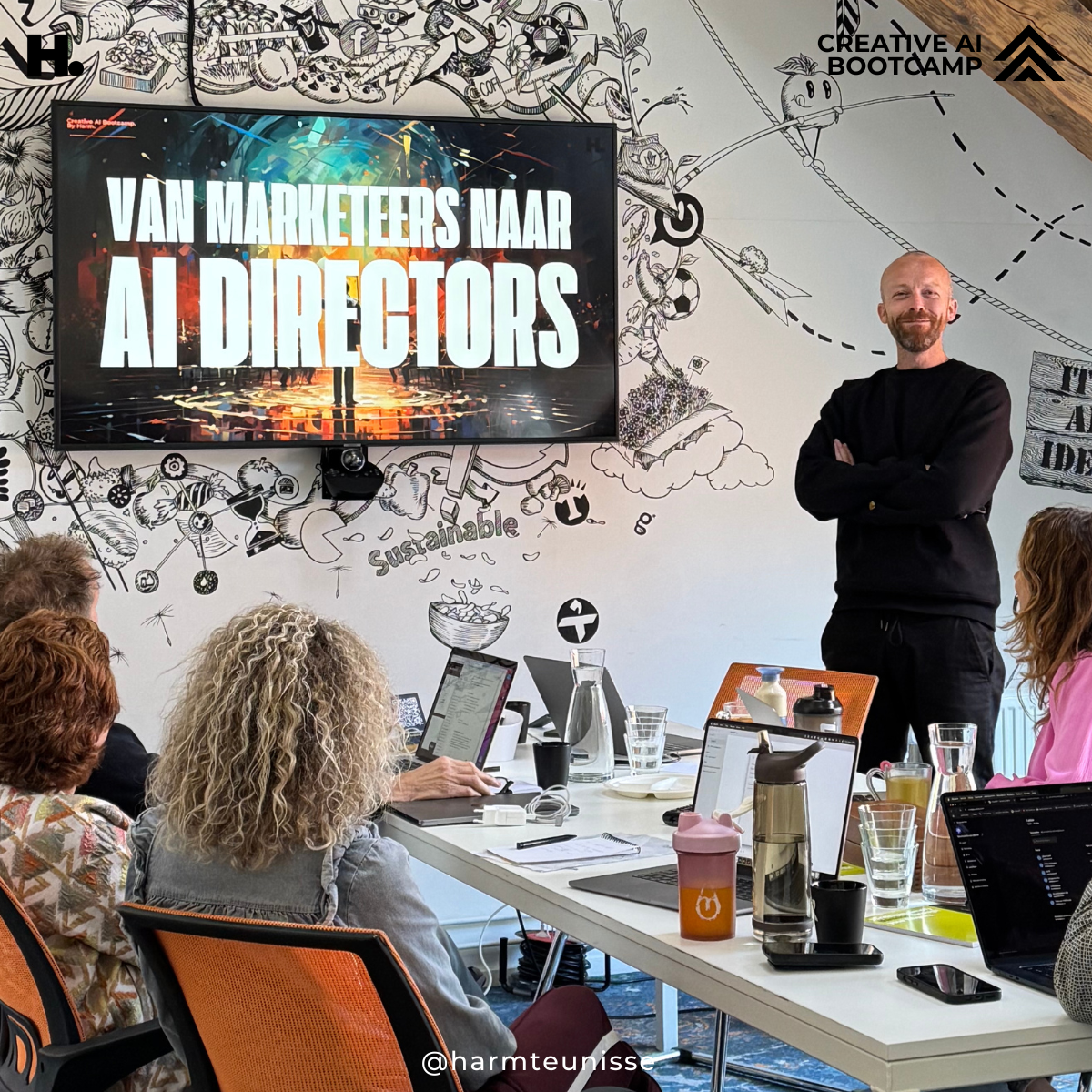 Een man staat voor een scherm met de tekst 'Van Marketeers Naar AI Directors' tijdens een presentatie in een vergaderruimte. Er zitten meerdere mensen aan tafel, met laptops, notitieblokken en drinken.