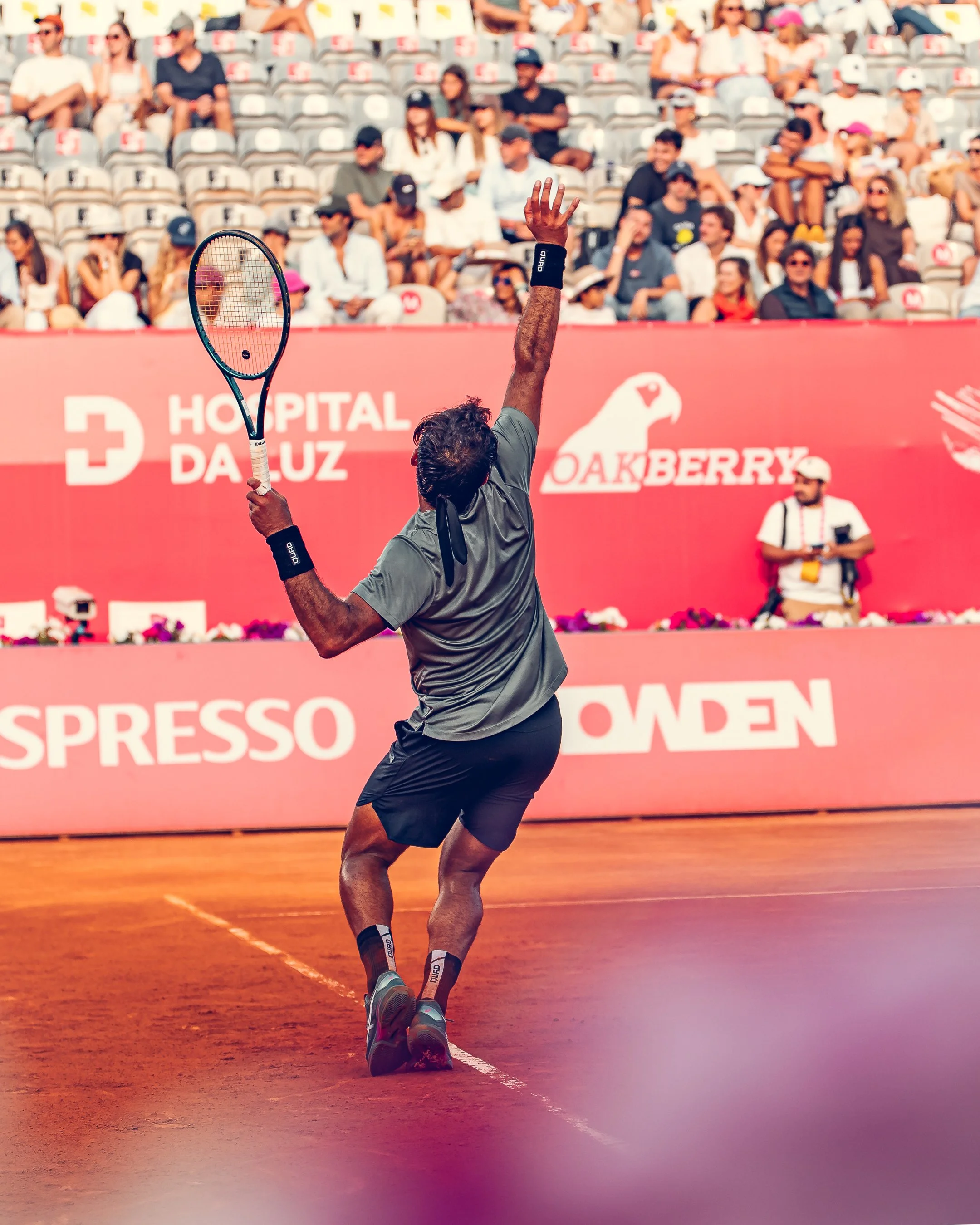 Tennis player in a gray shirt and black shorts, barefoot, hitting a tennis ball on a clay court during a match at the Adelaide International.