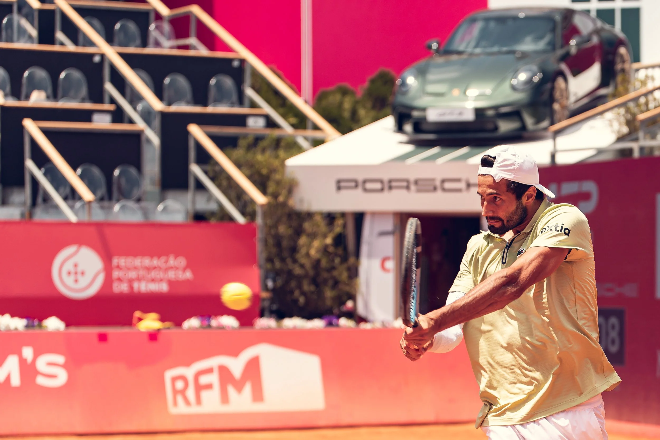 A tennis player is preparing to hit a tennis ball on a court during a match. The background shows sponsor banners and a scoreboard.