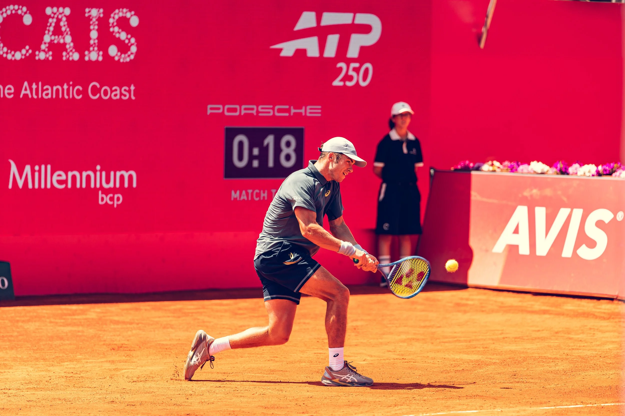 A tennis player in sportswear is hitting a tennis ball with a racket on a clay court during a match on a sunny day.