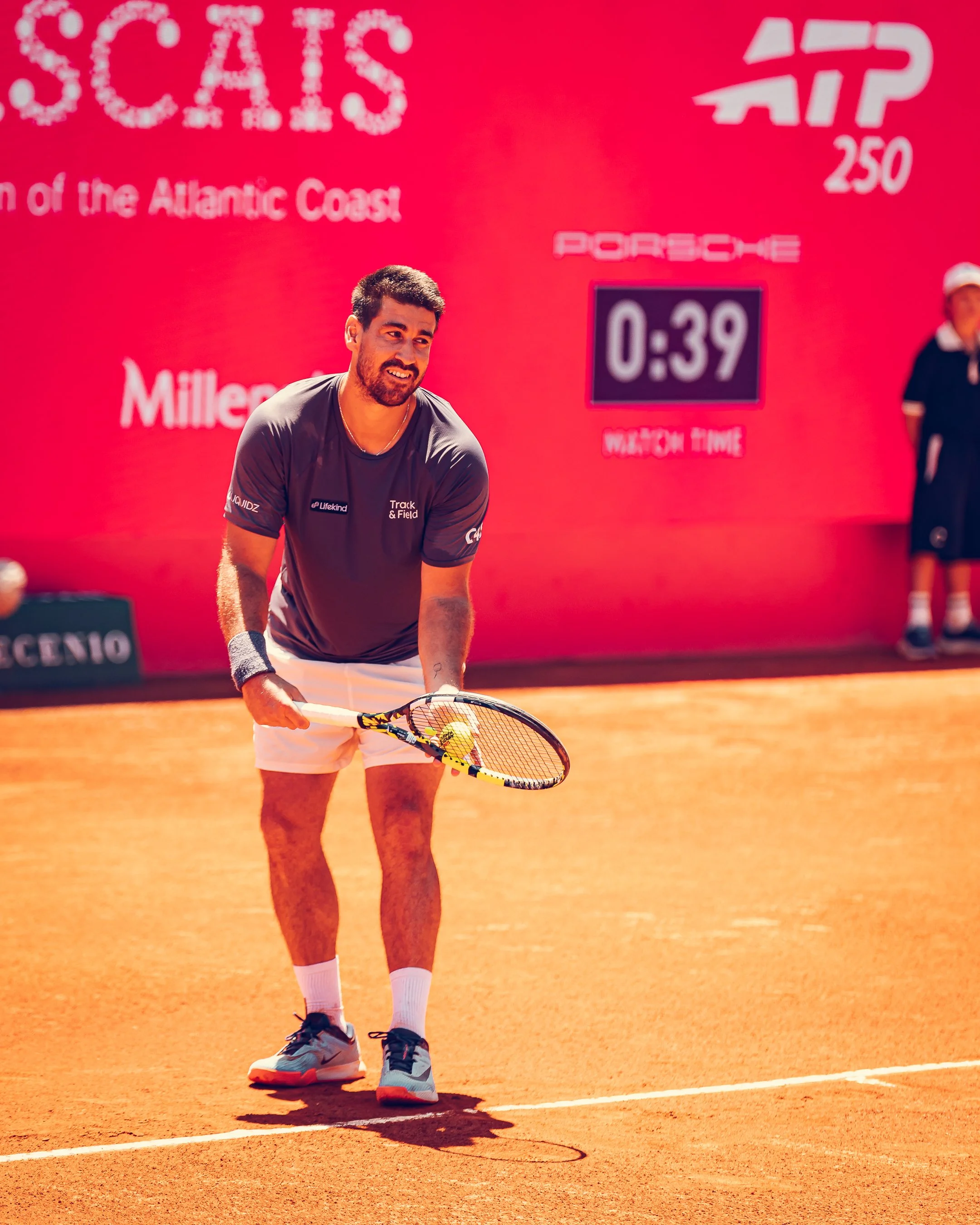 Tennis player holding a racket on a clay court, with a large red scoreboard in the background displaying a match time of 0:39.