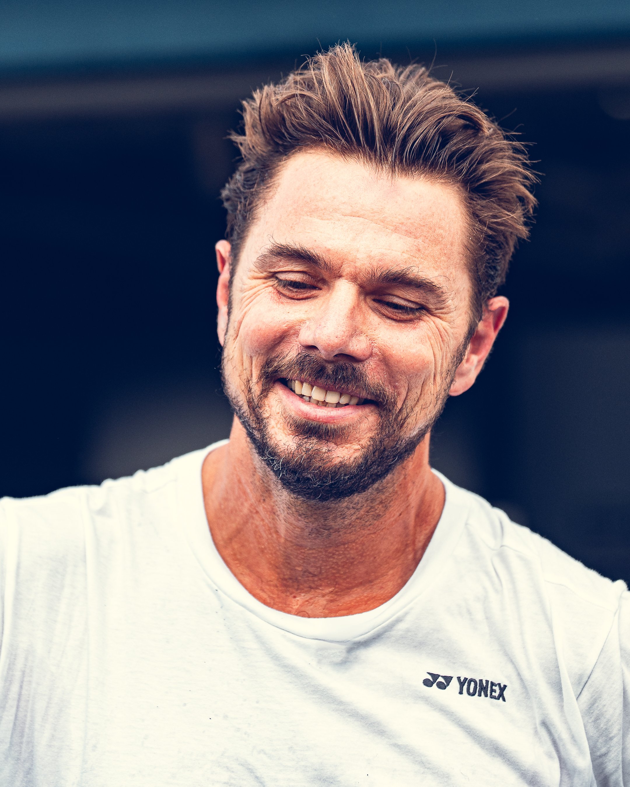 A man smiling, wearing a white Yonex sports shirt.