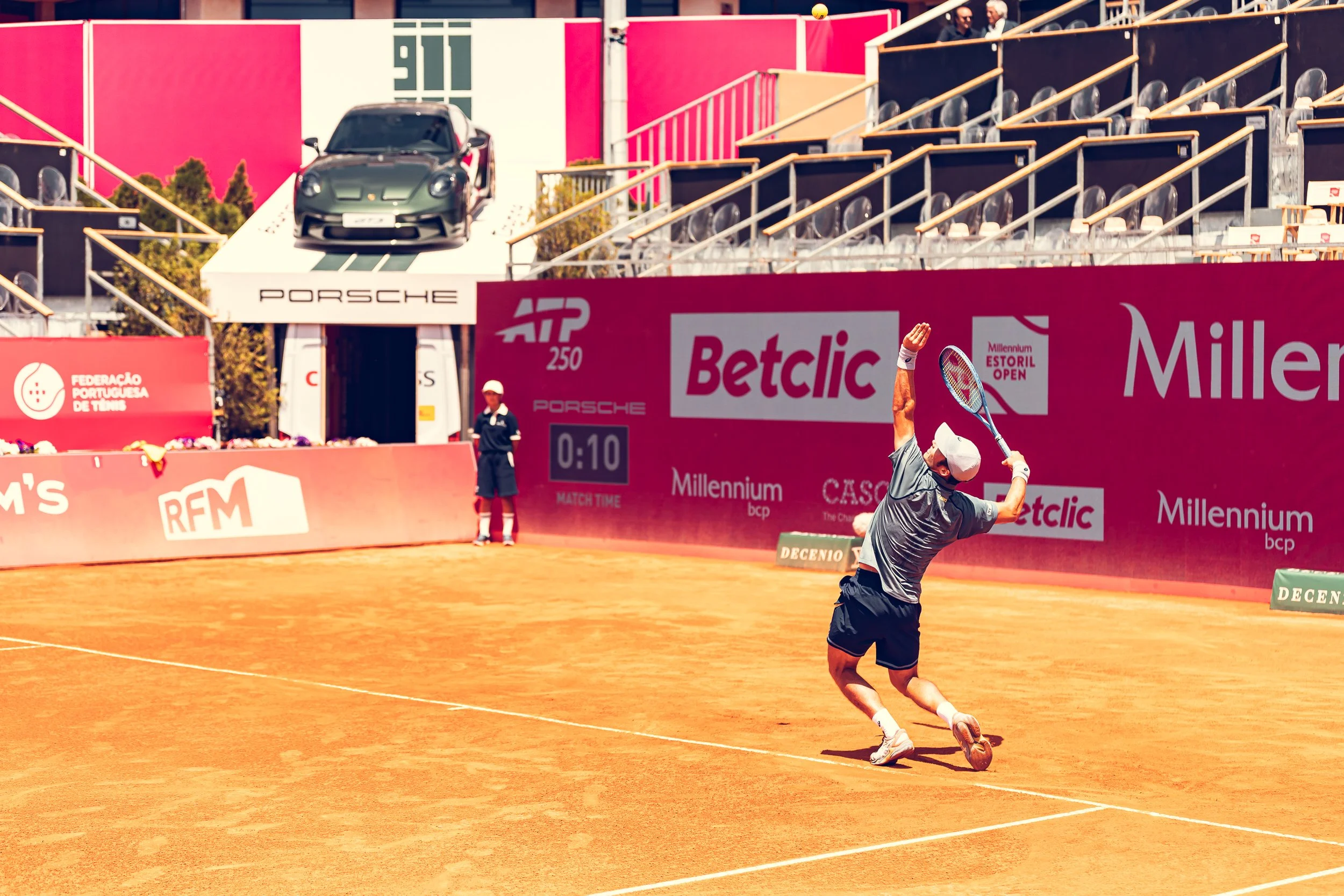 A male tennis player is seen tilting back and preparing to hit a tennis ball with his racket on a clay court during a match, with a pink advertising wall in the background.