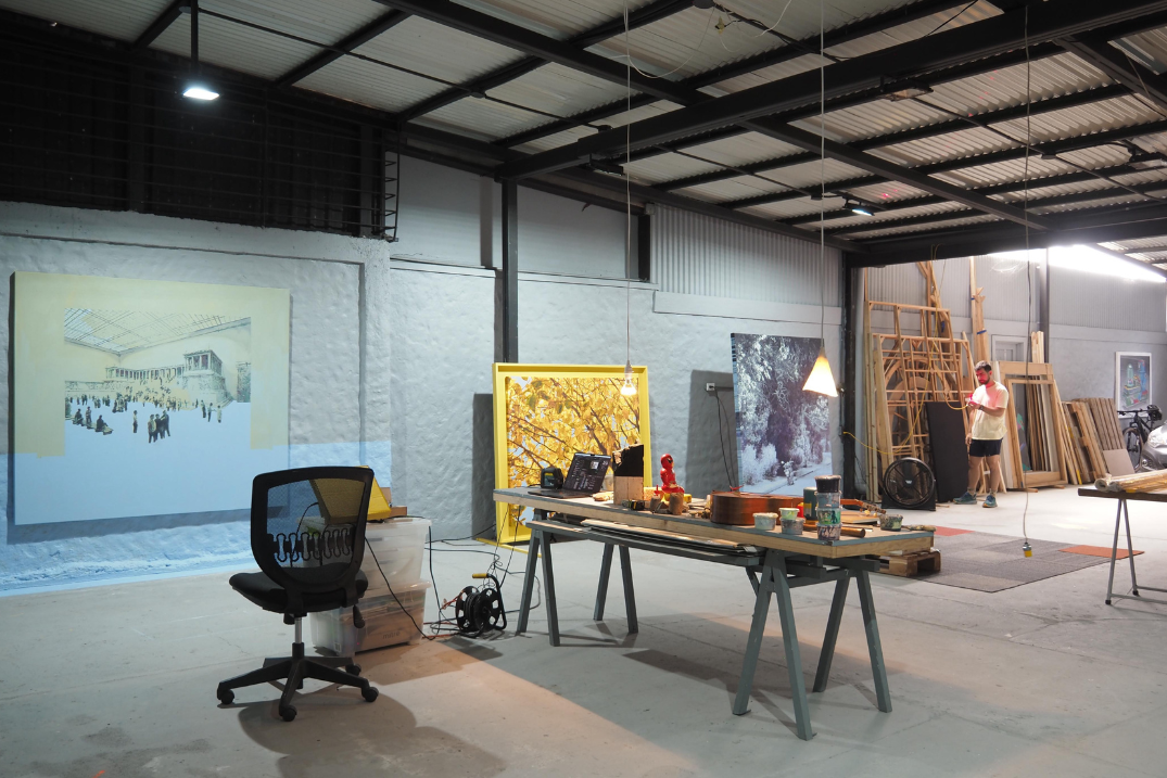 Image of a dimly lit work studio with canvases and finished paintings rusting up against the walls