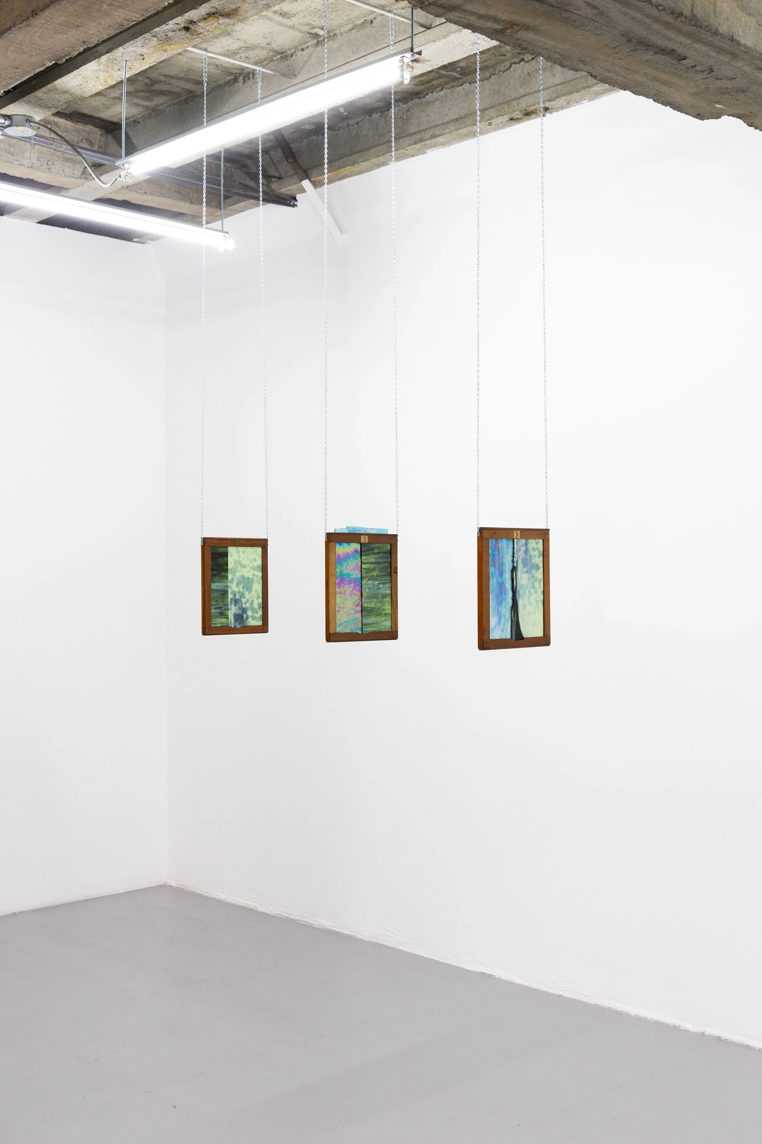 three hanging wooden framed stained glass art pieces in gallery space