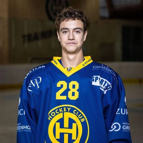 Ein junger Mann in einem blauen Eishockey-Trikot mit der Nummer 28, stehend auf einer Eishockeybahn.