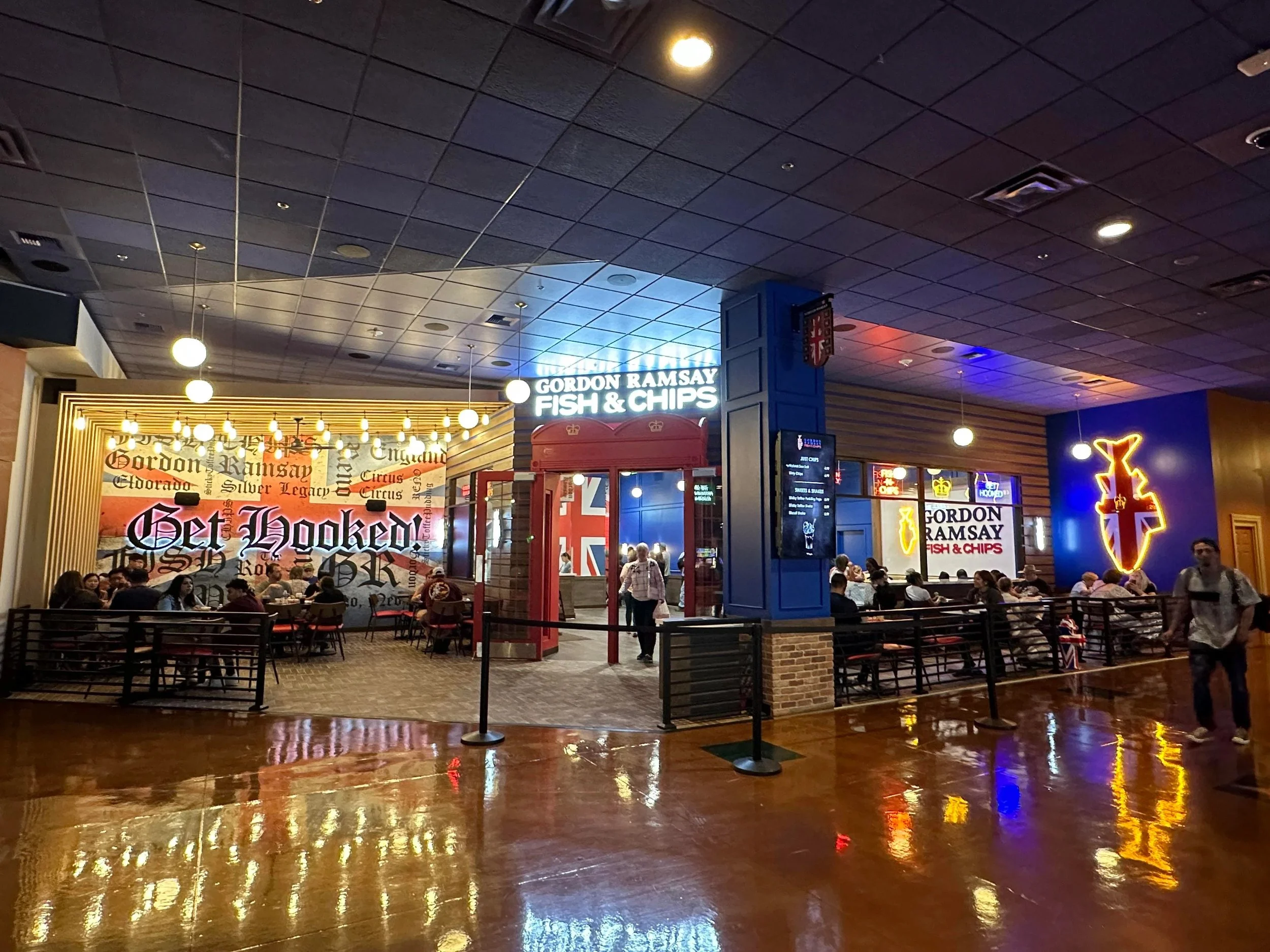 Inside Gordon Ramsay Fish & Chips restaurant with neon and illuminated signs, seating areas, and patrons dining.