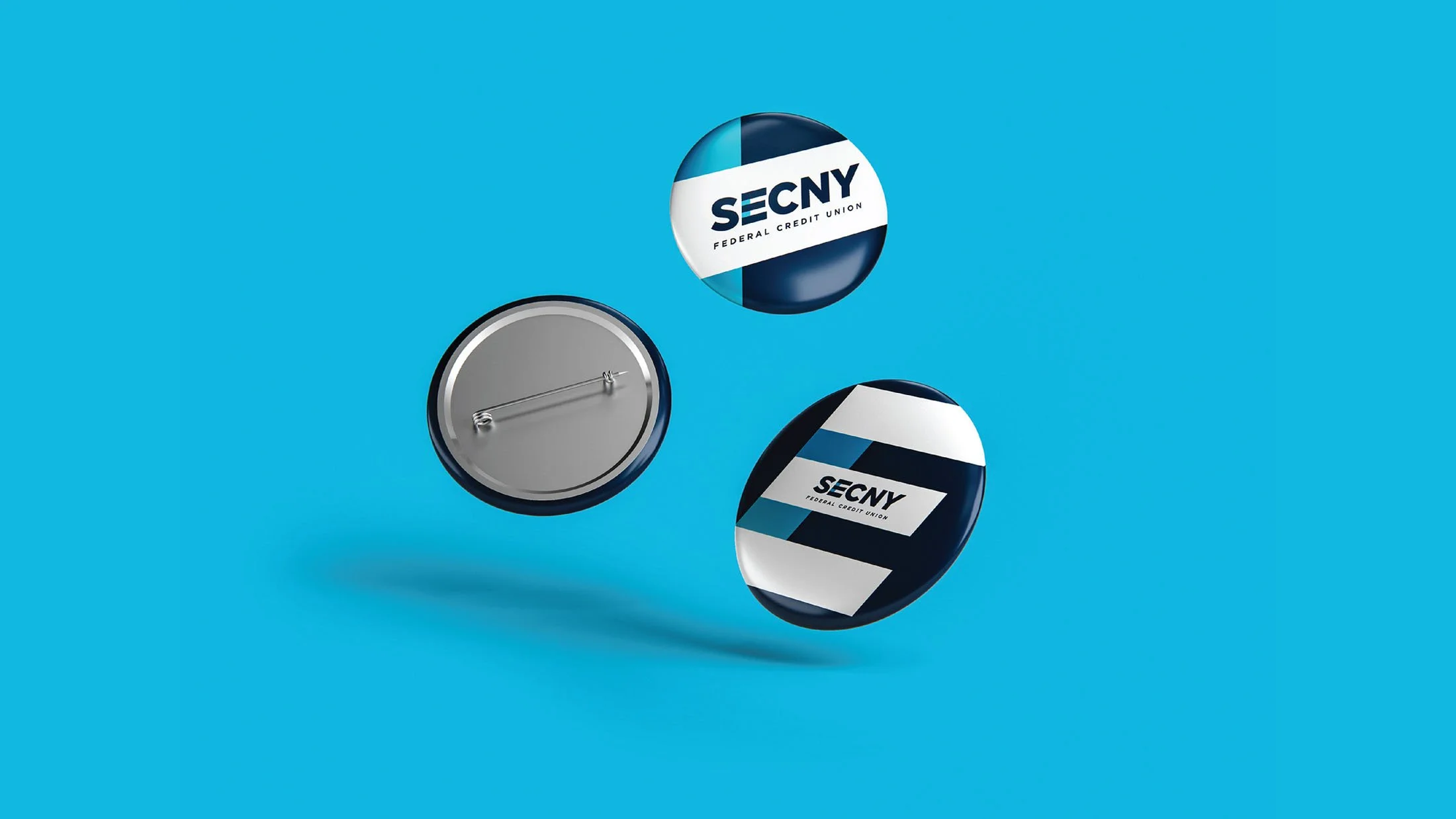 CINSYR | Creative design agency Syracuse, New York | SECNY federal credit union brand identity branded SECNY button pins three falling in the air