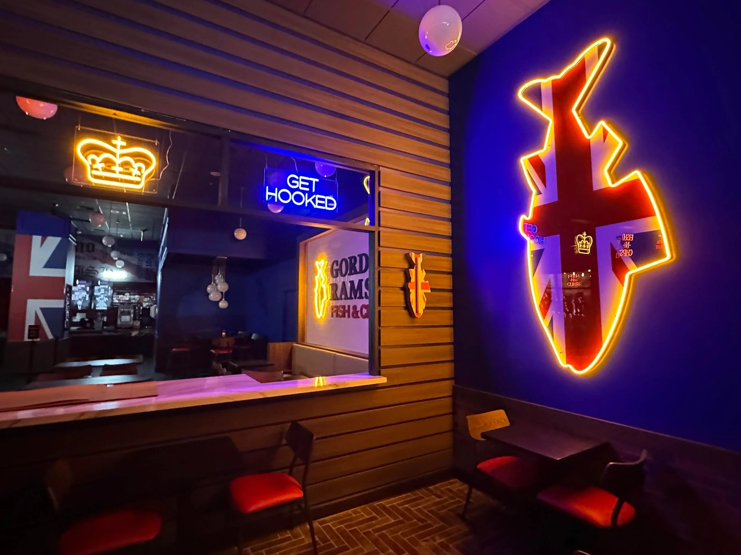 Neon signs in a bar featuring a crown, the text 'GET HOOKED', and a large neon outline of the country of England with the Union Jack flag inside.