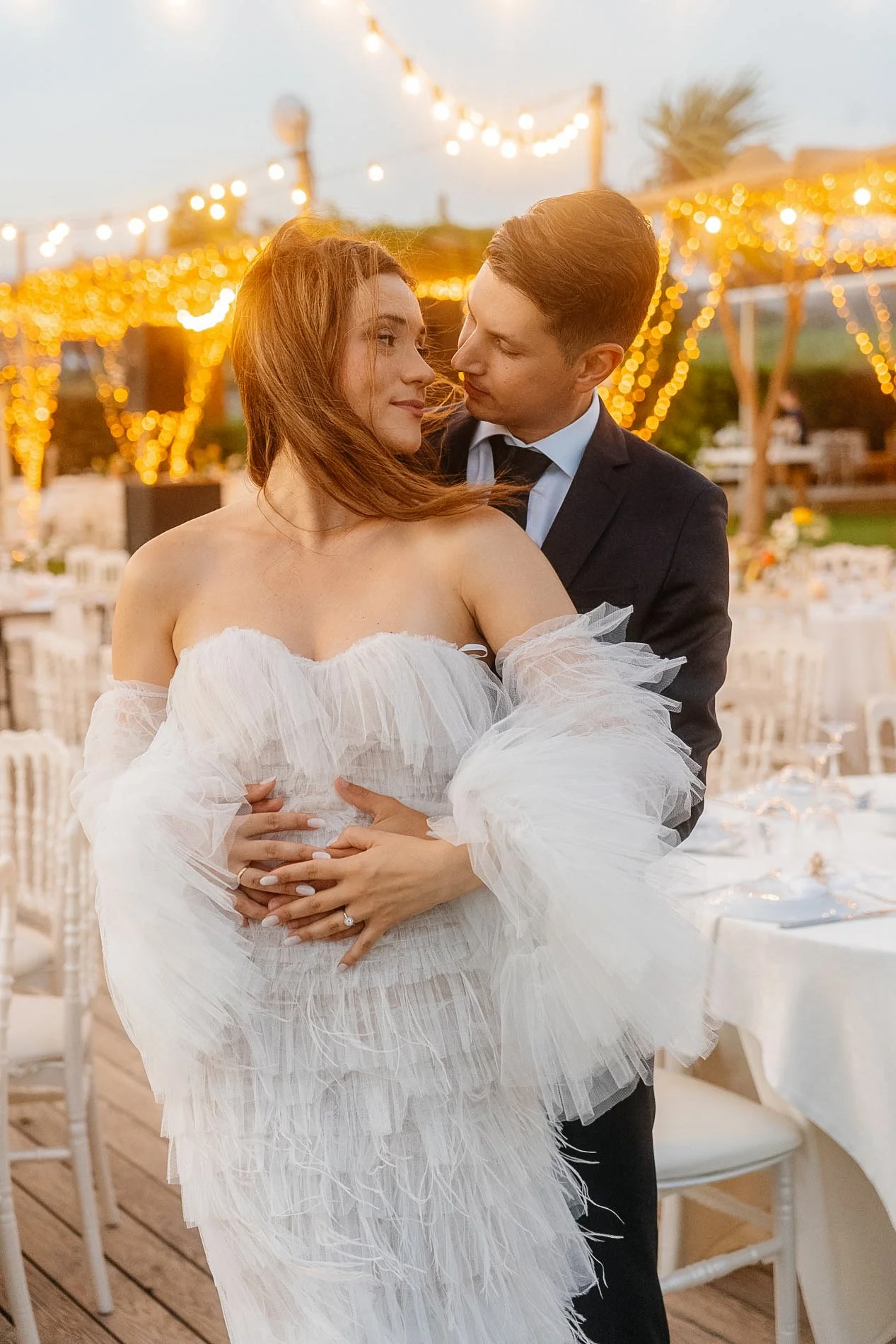 A bride and groom sharing a dance at an outdoor wedding reception decorated with string lights and elegant tables.