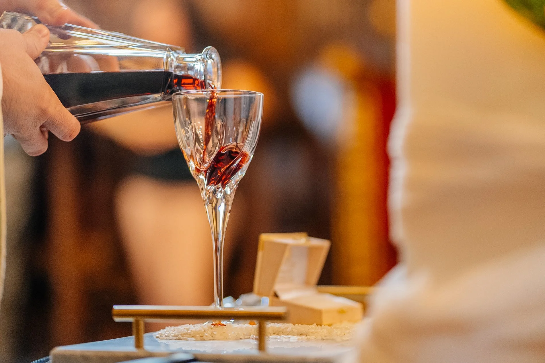 A person pouring red wine from a bottle into a glass on a table.