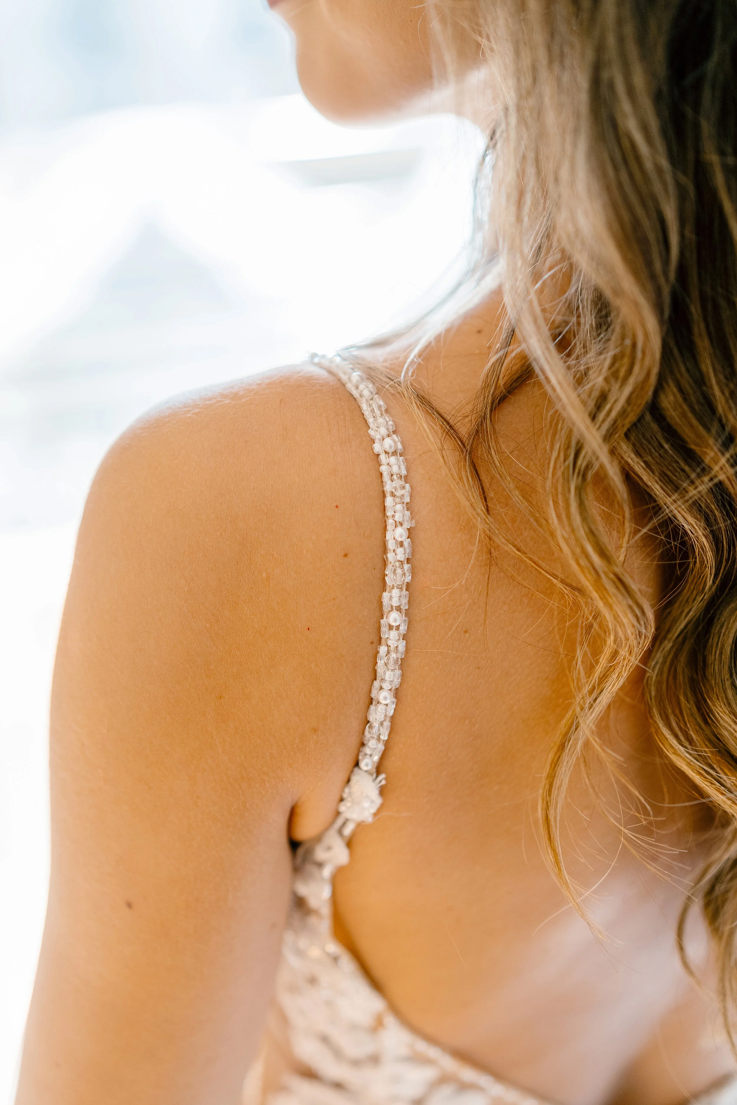 Close-up of a woman's shoulder and part of her face, with curly hair and a sleeveless dress with sparkling embellishments