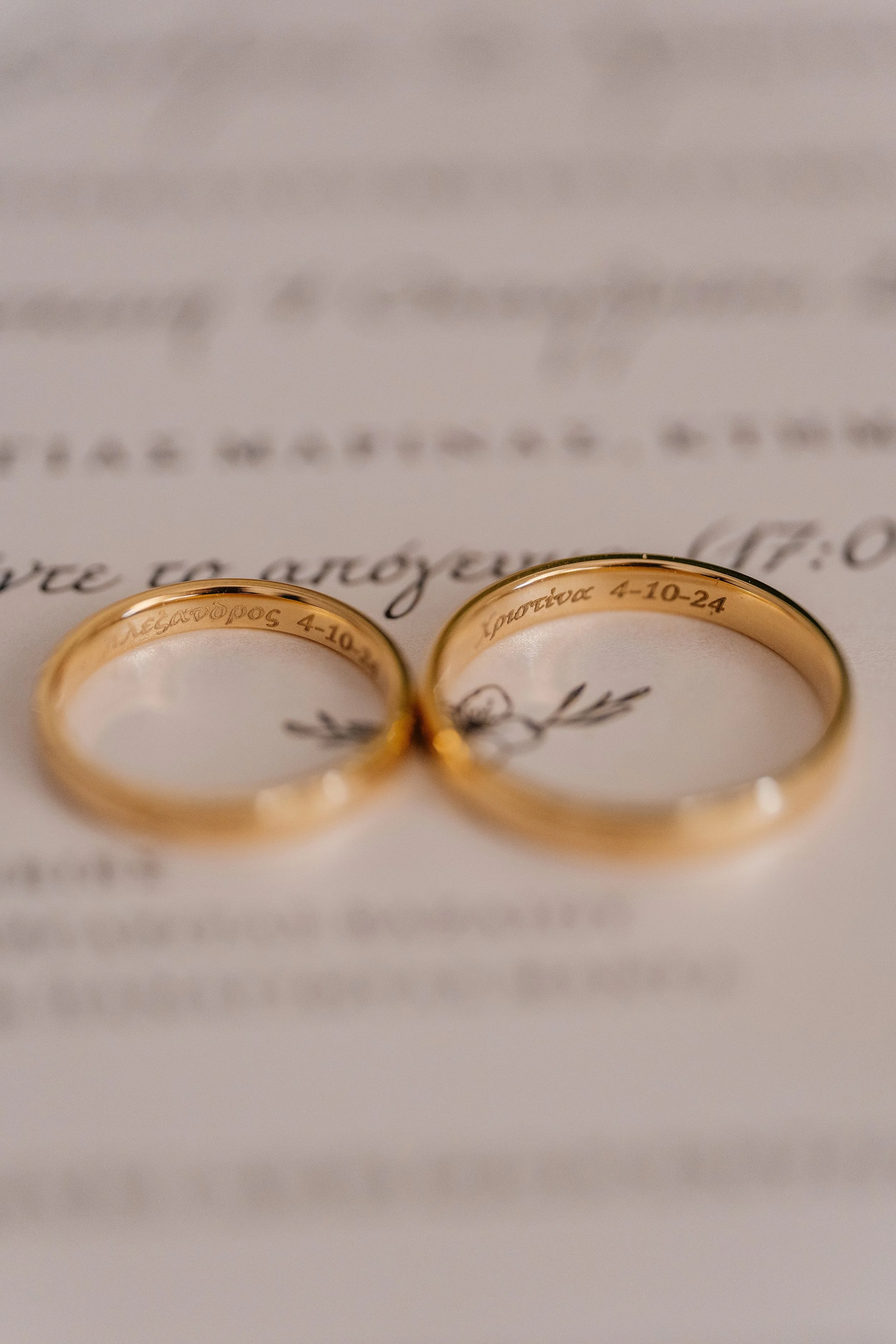 Close-up of two gold wedding rings with engraved dates and names, placed on a white background with cursive writing.