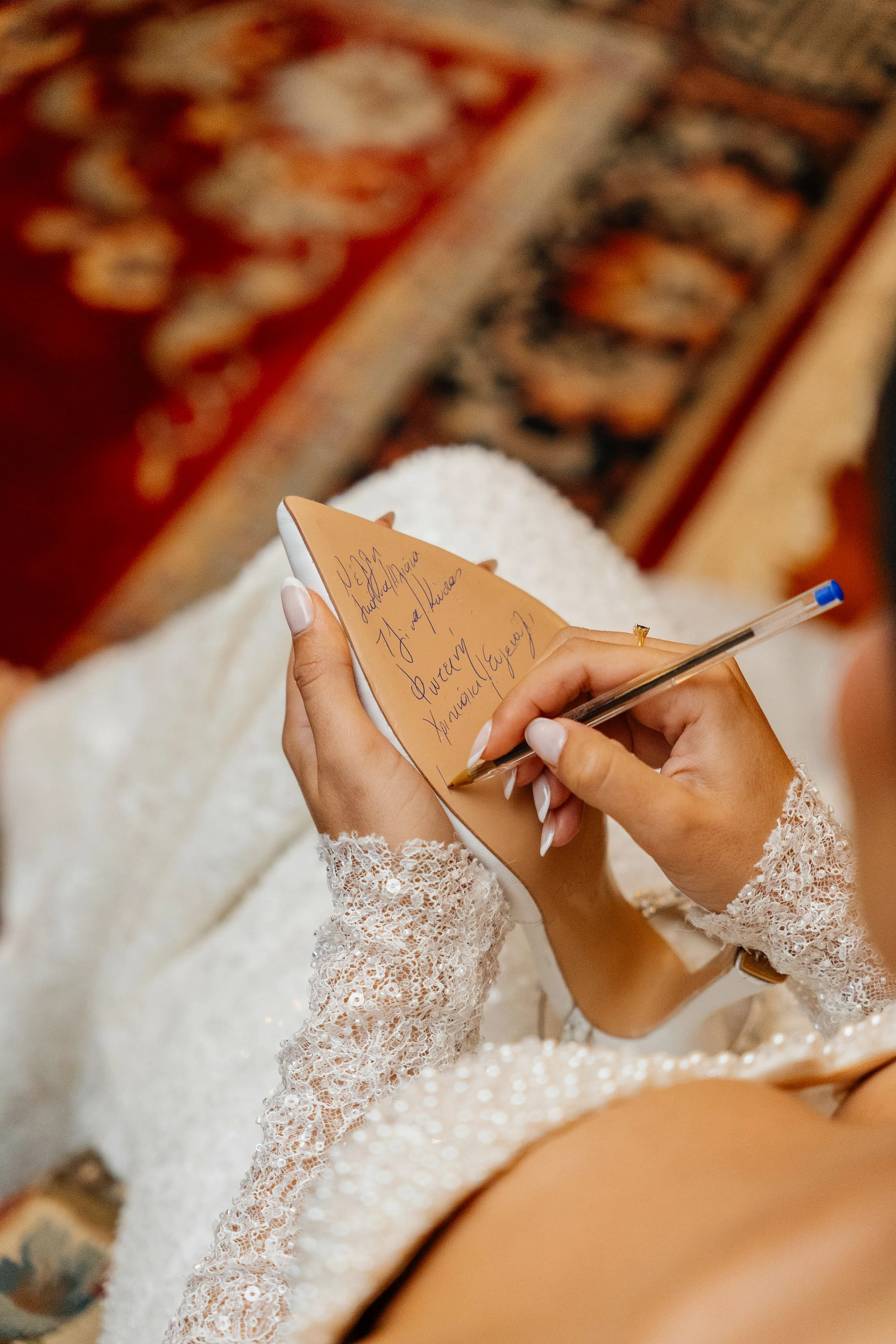 A person in a lace long-sleeve dress is writing on a small notepad with a pen, likely at a wedding or special event.
