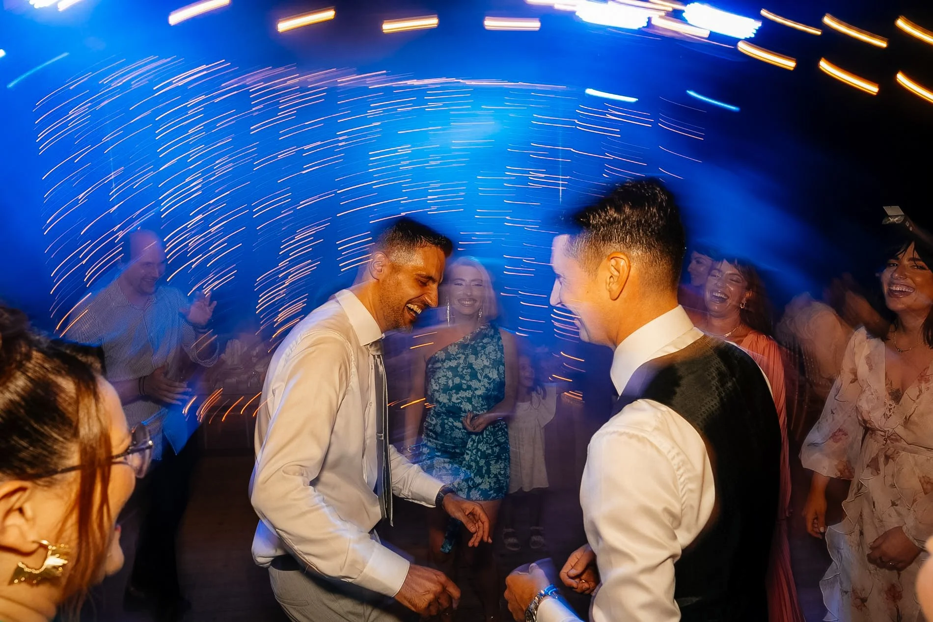 People dancing and celebrating at a party with colorful light trails in the background.