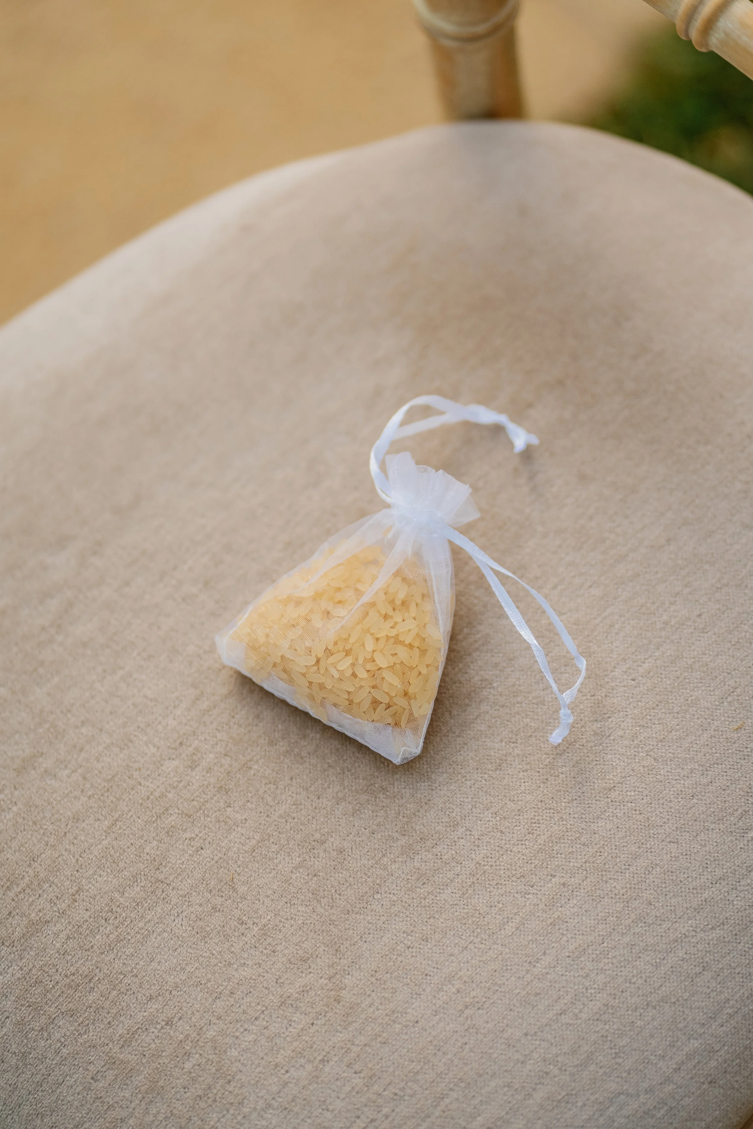Small organza bag filled with rice, tied with a white ribbon, placed on a beige surface.