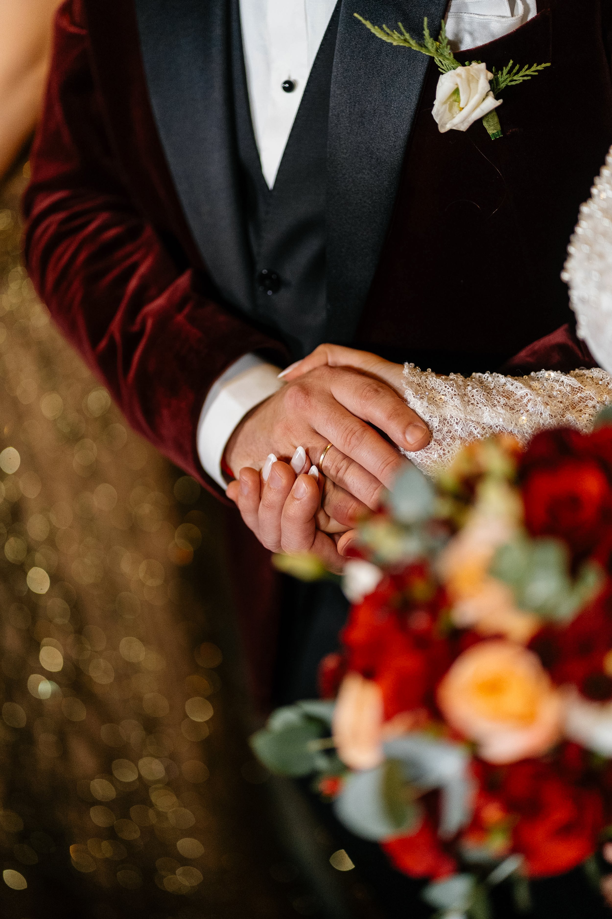 Close-up of a bride and groom holding hands during a wedding ceremony, with blurred background.