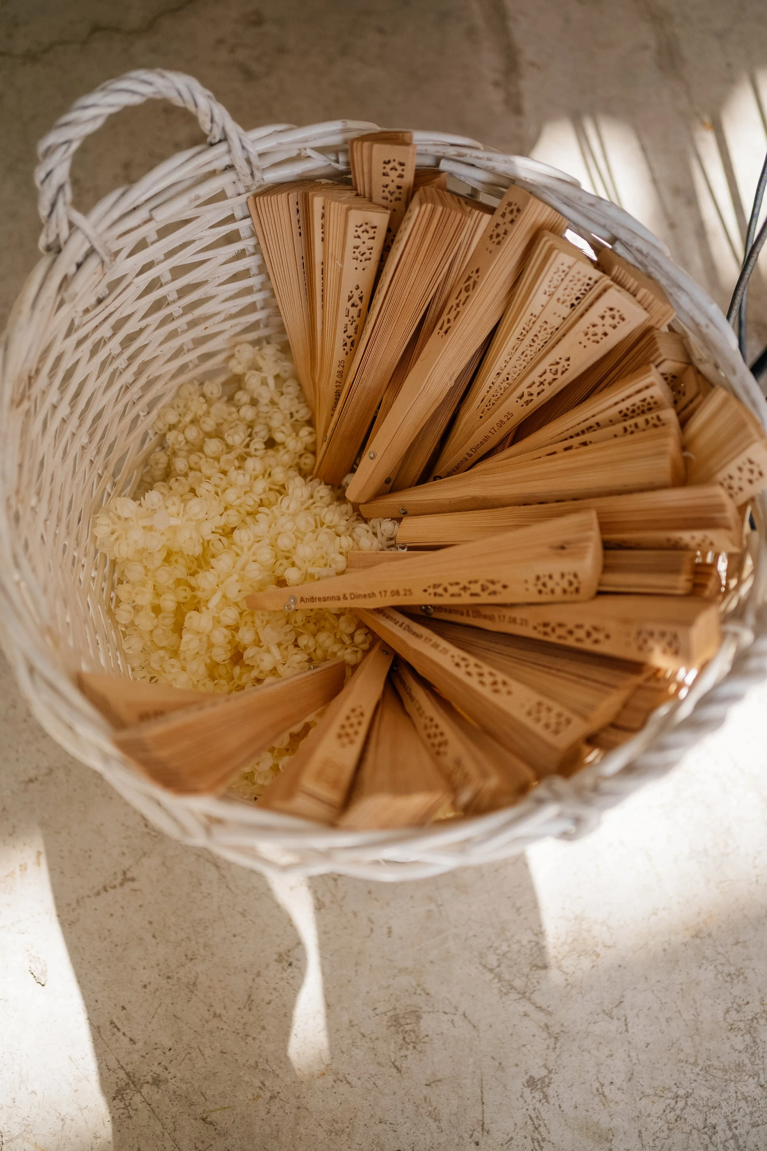 A white wicker basket containing wooden fans and small white flowers, with a concrete floor in the background.