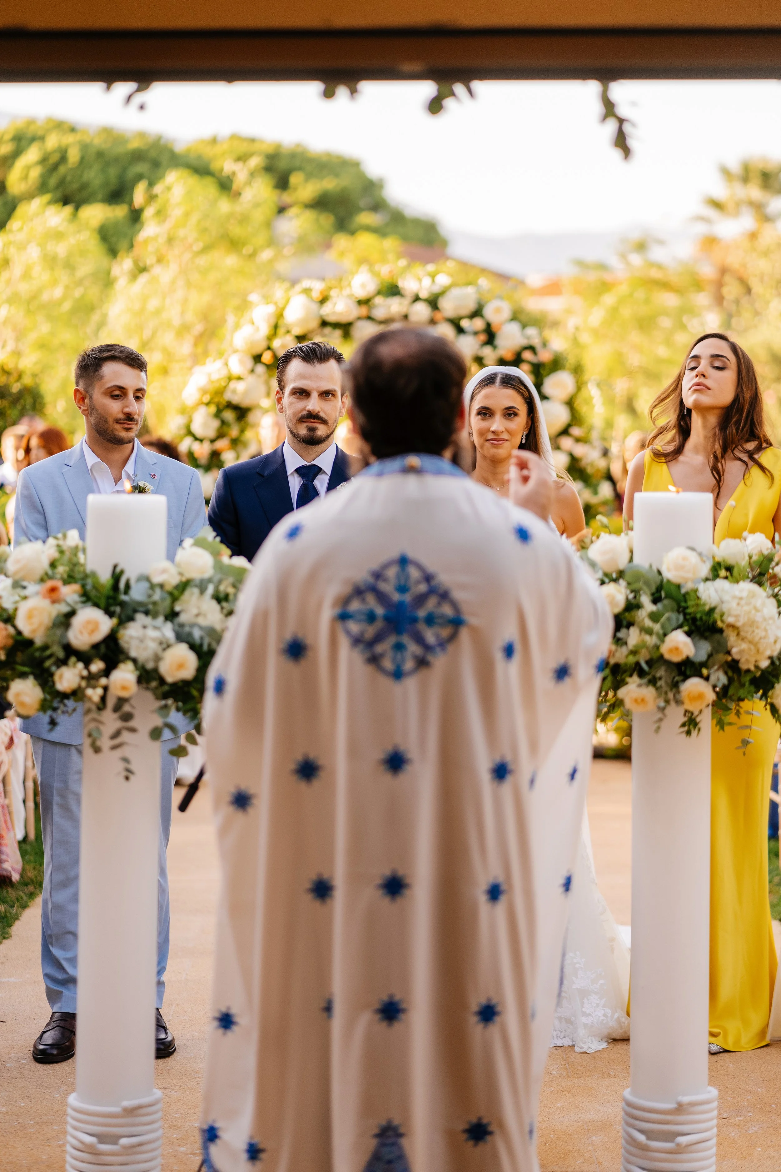 A wedding ceremony outdoors with four people standing behind a floral altar, with candles and greenery, as the officiant faces the couple.