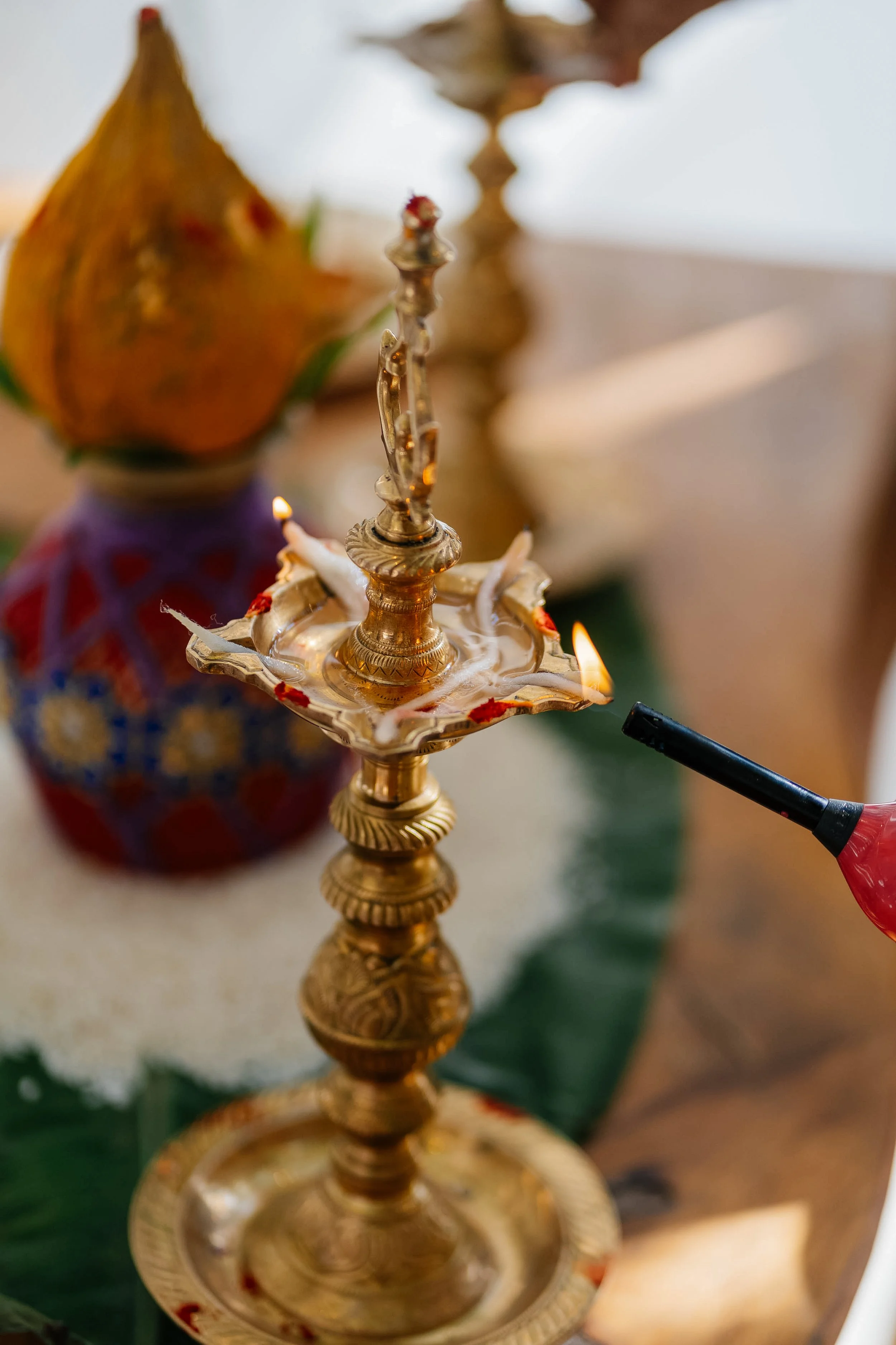 A brass lamp stand with lit candles and a blurred background with a decorative orange and purple container.
