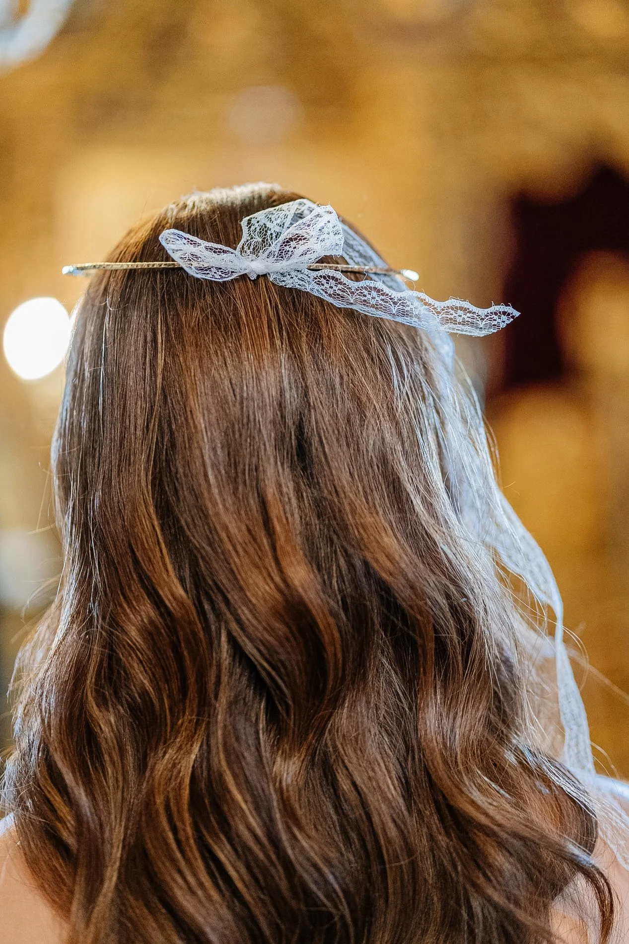 A person with long, wavy, auburn hair wearing a lace bow headband, viewed from behind.